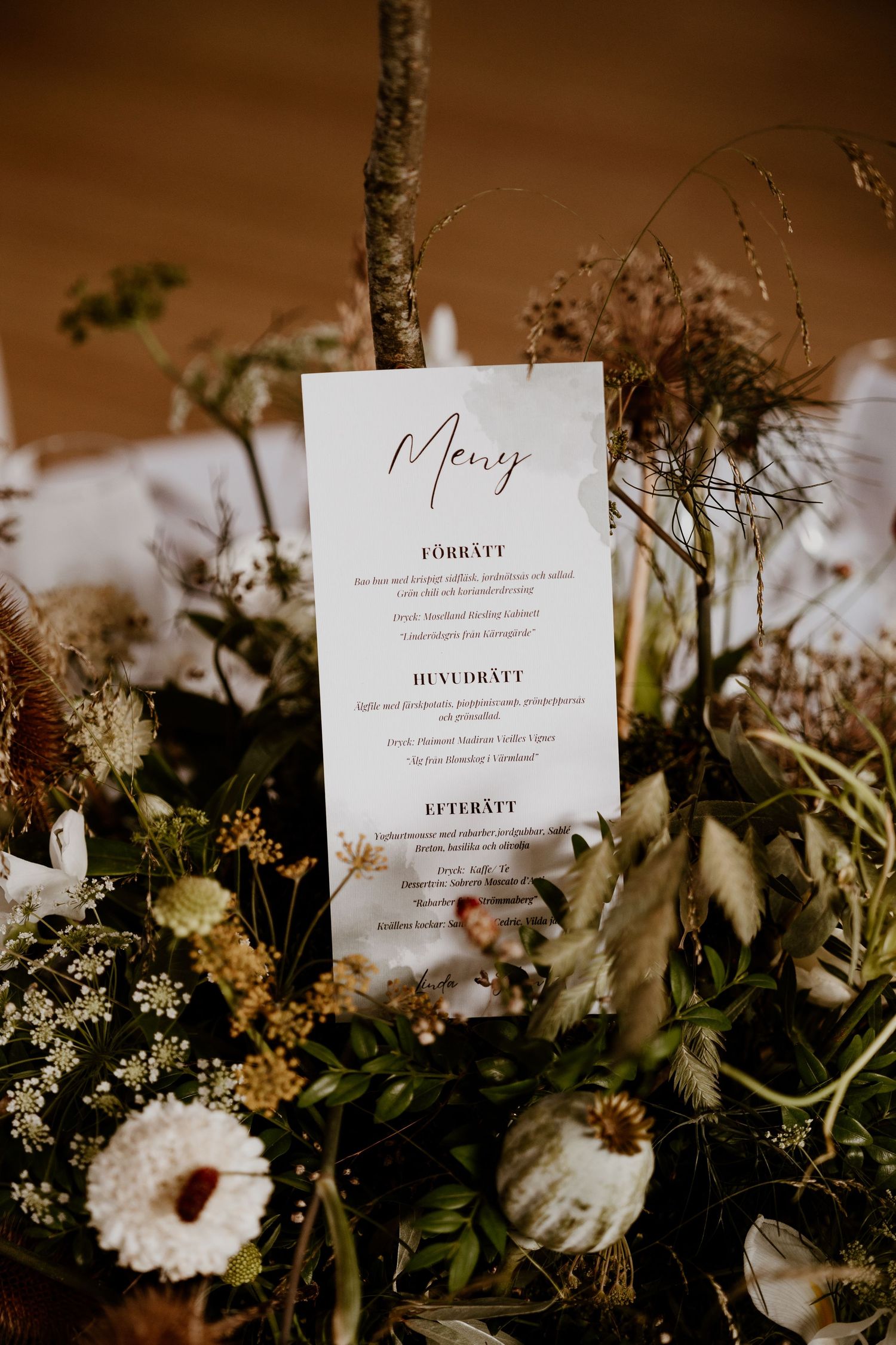 A series of elegant wedding menu cards displayed among fresh wildflowers and greenery in warm lighting.
