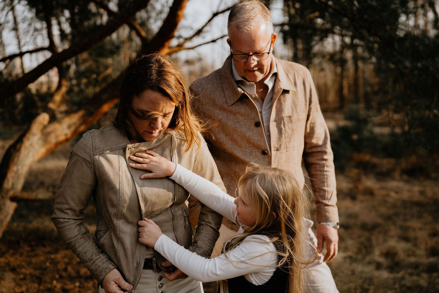 Family enjoys tender moment together in warm sunlit forest during sunset golden hour.