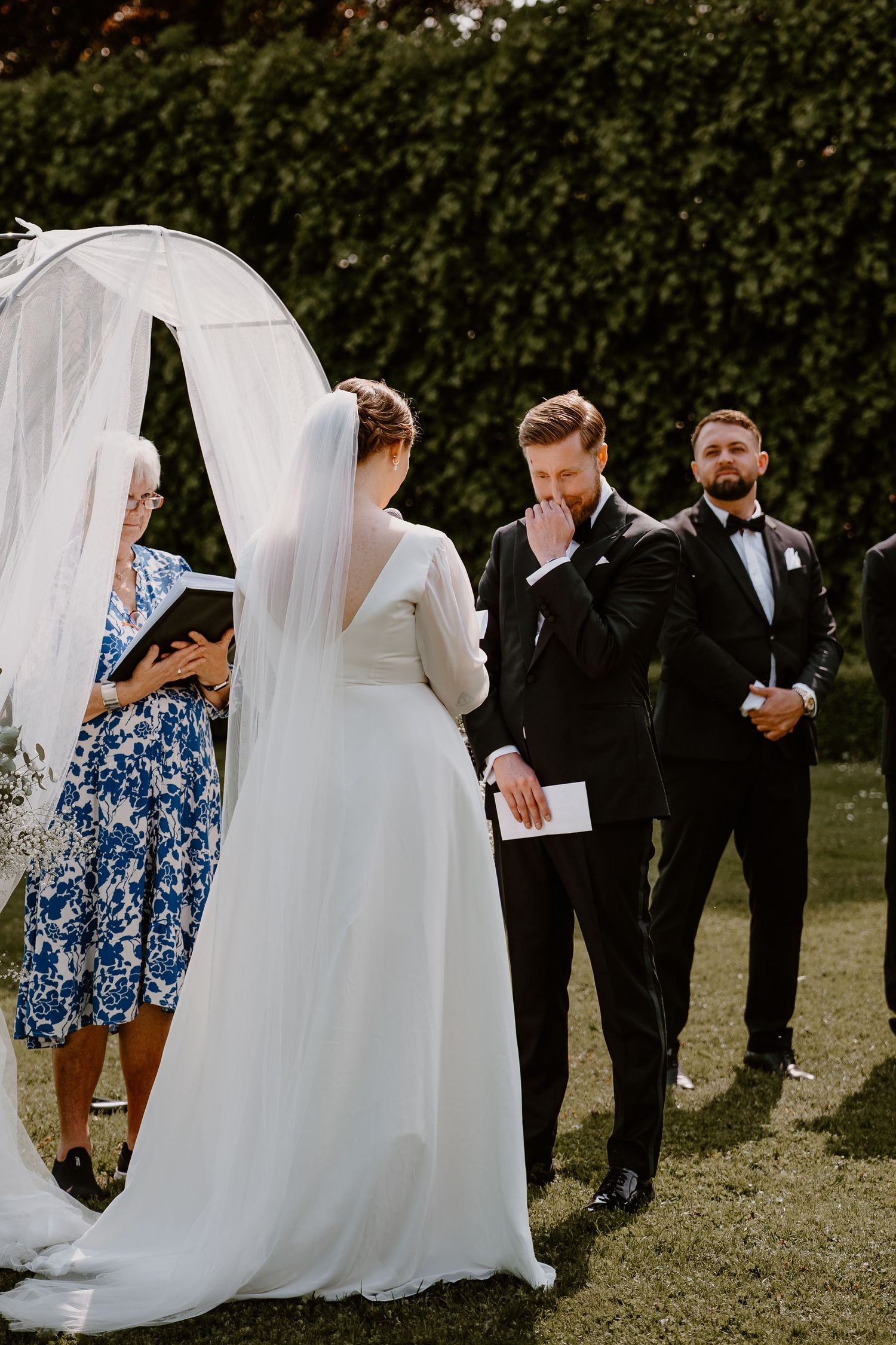 A series of candid wedding party photos showing guests in formal attire interacting with a flowing white wedding dress on grass.