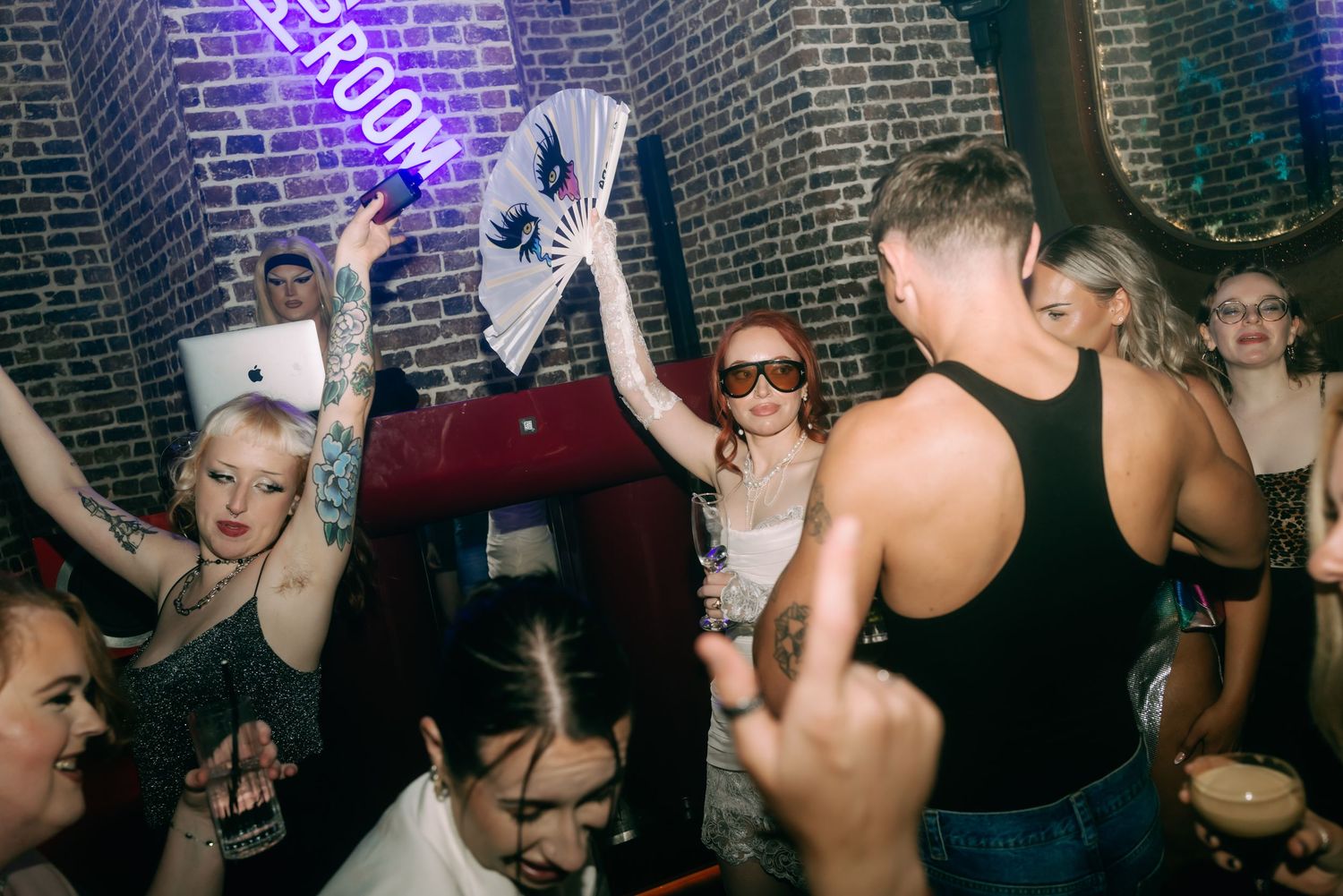 People dancing and socializing at a crowded nightclub with purple lighting and brick walls.