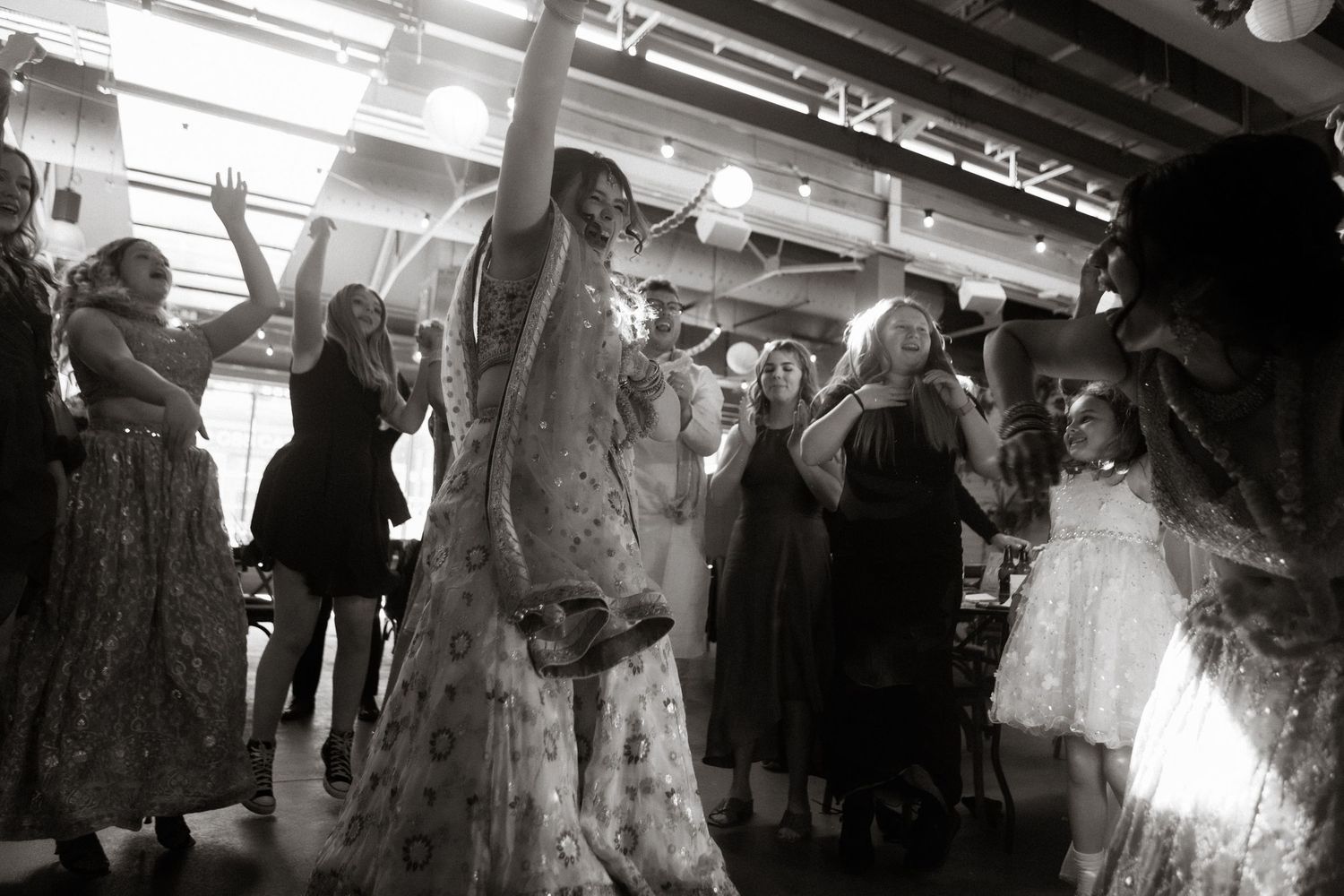 A black and white photo shows people dancing and celebrating in a crowded indoor venue with low ceilings.