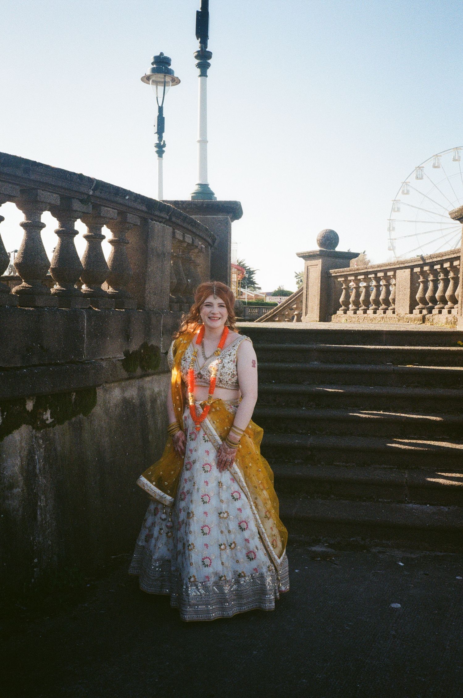 Someone wearing a floral printed dress poses on stone steps with a vintage street lamp and ferris wheel visible in background.