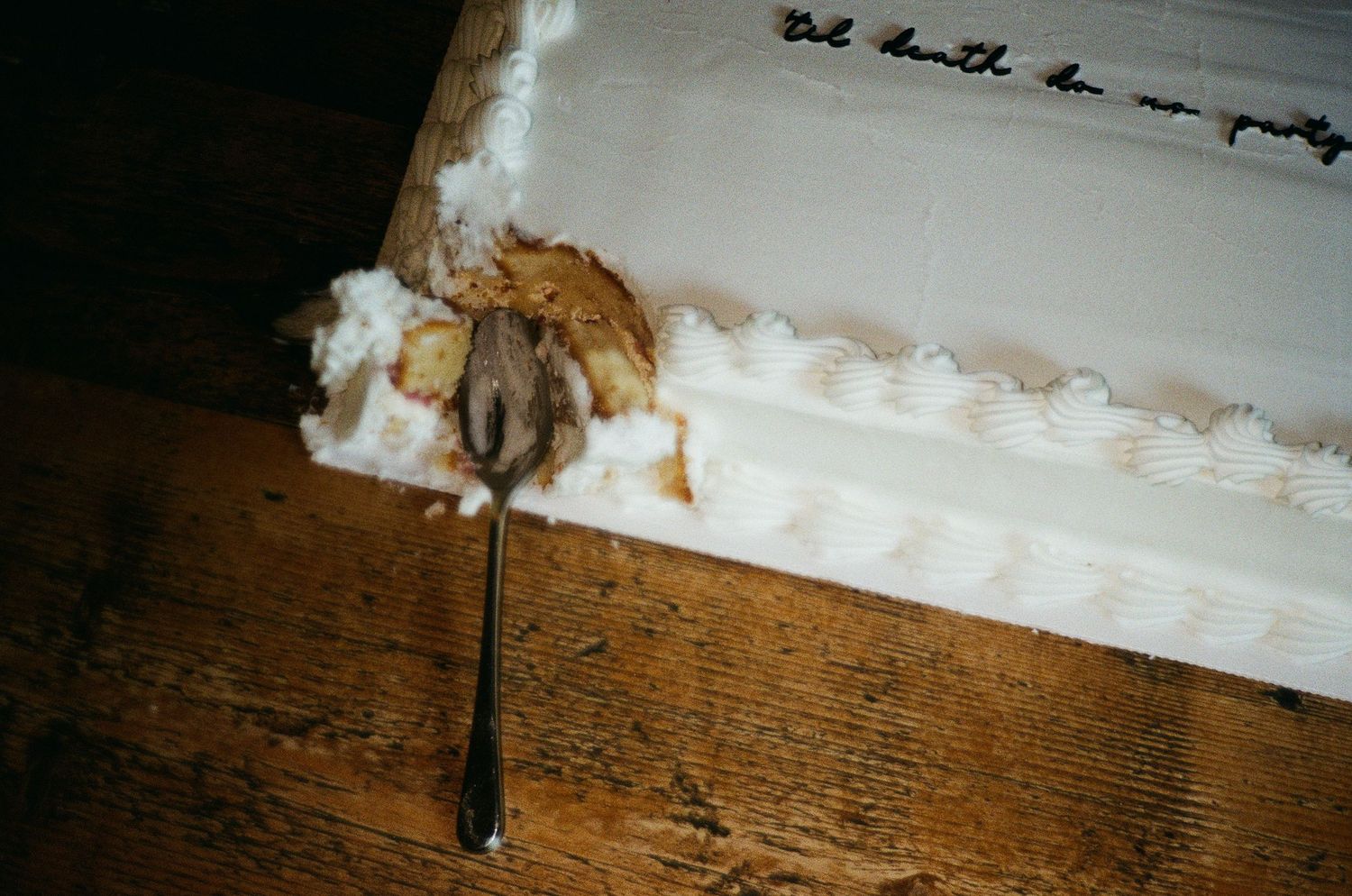 A spoon with melted chocolate smears rests on a rustic wooden surface next to white frosting.