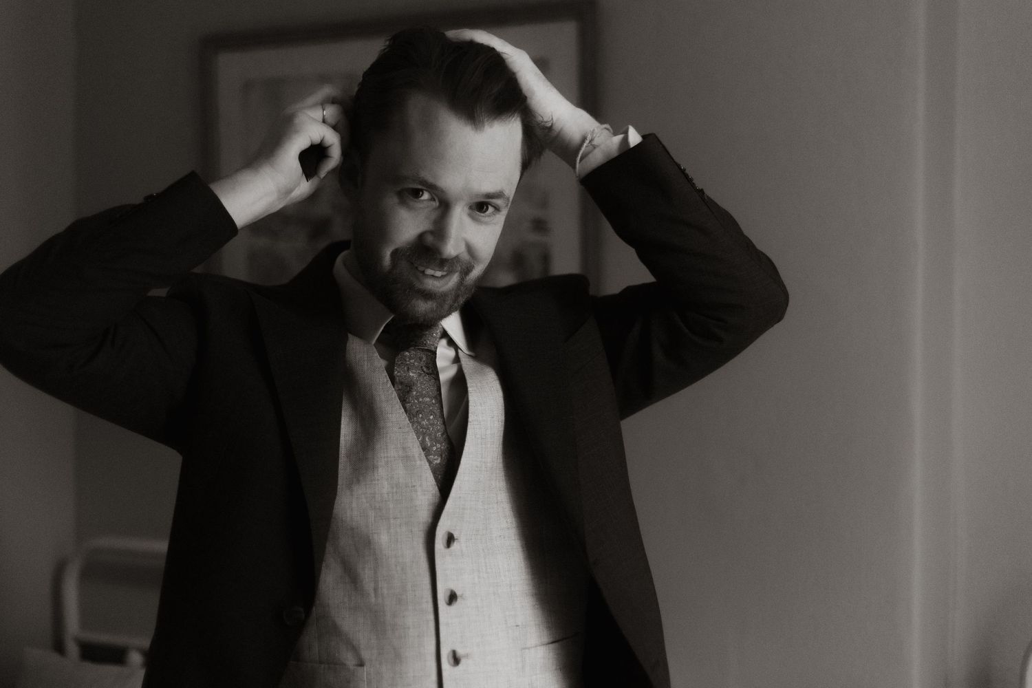 Black and white portrait of someone in formal attire running hands through hair in dramatic lighting.