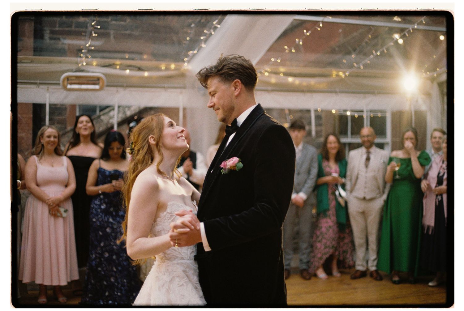 Bride and groom share first dance at elegant wedding reception with guests watching in background.
