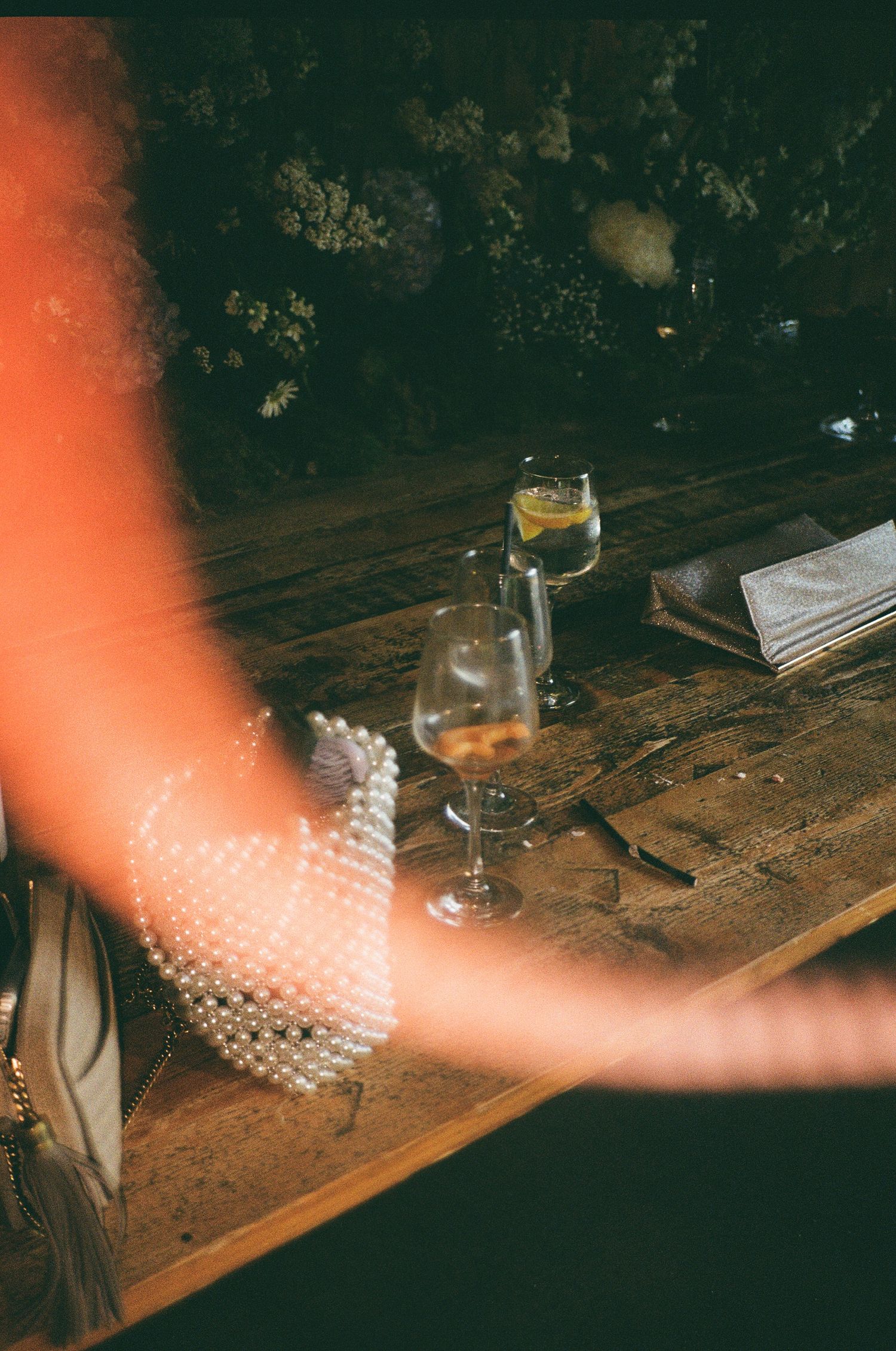 A blurred arm in motion reaches across a rustic wooden table with wine glasses and ambient lighting.