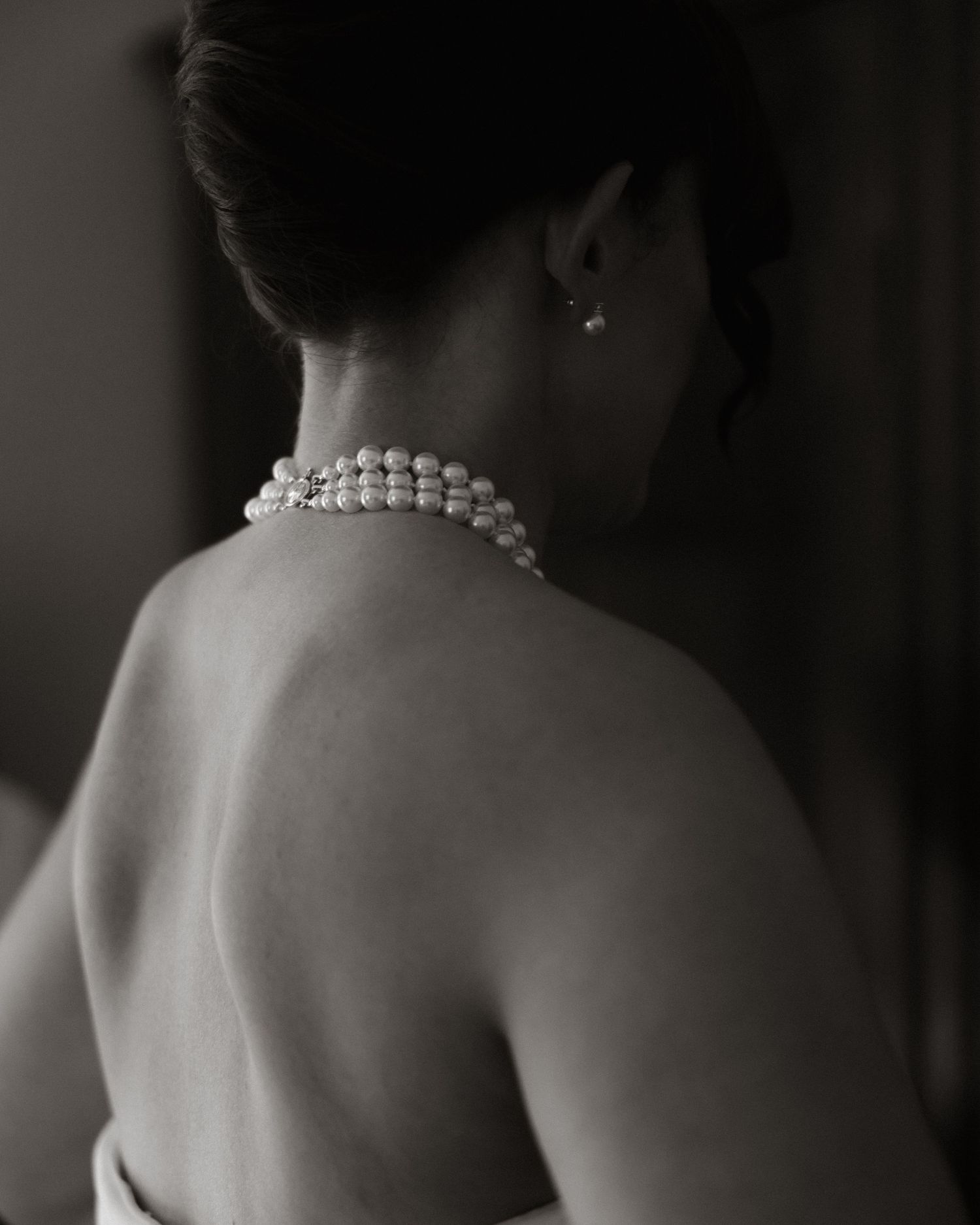Classic black and white portrait showing a bare back adorned with a delicate pearl necklace.