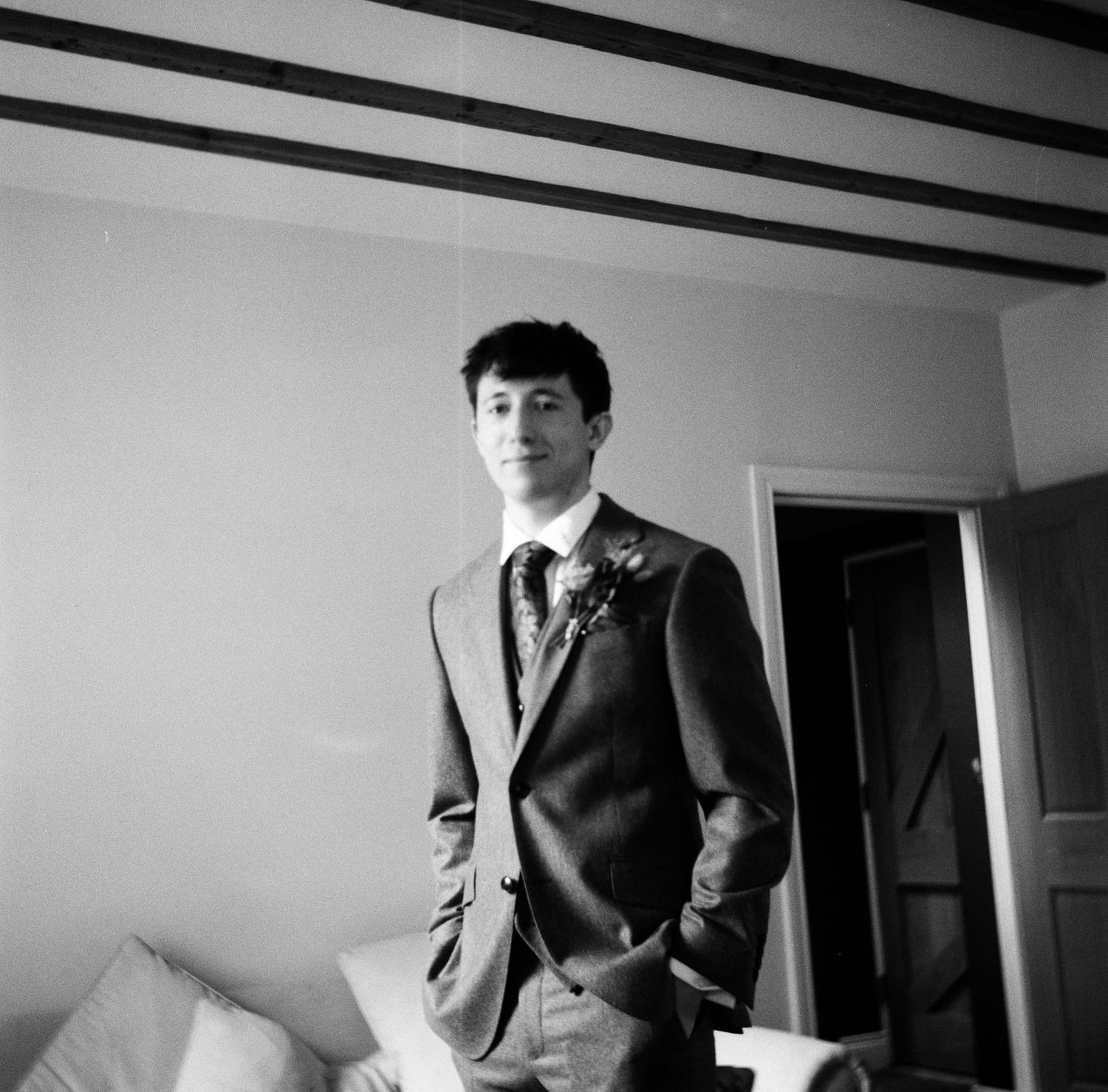 Black and white photograph of a person in a formal suit and tie standing in an interior room.