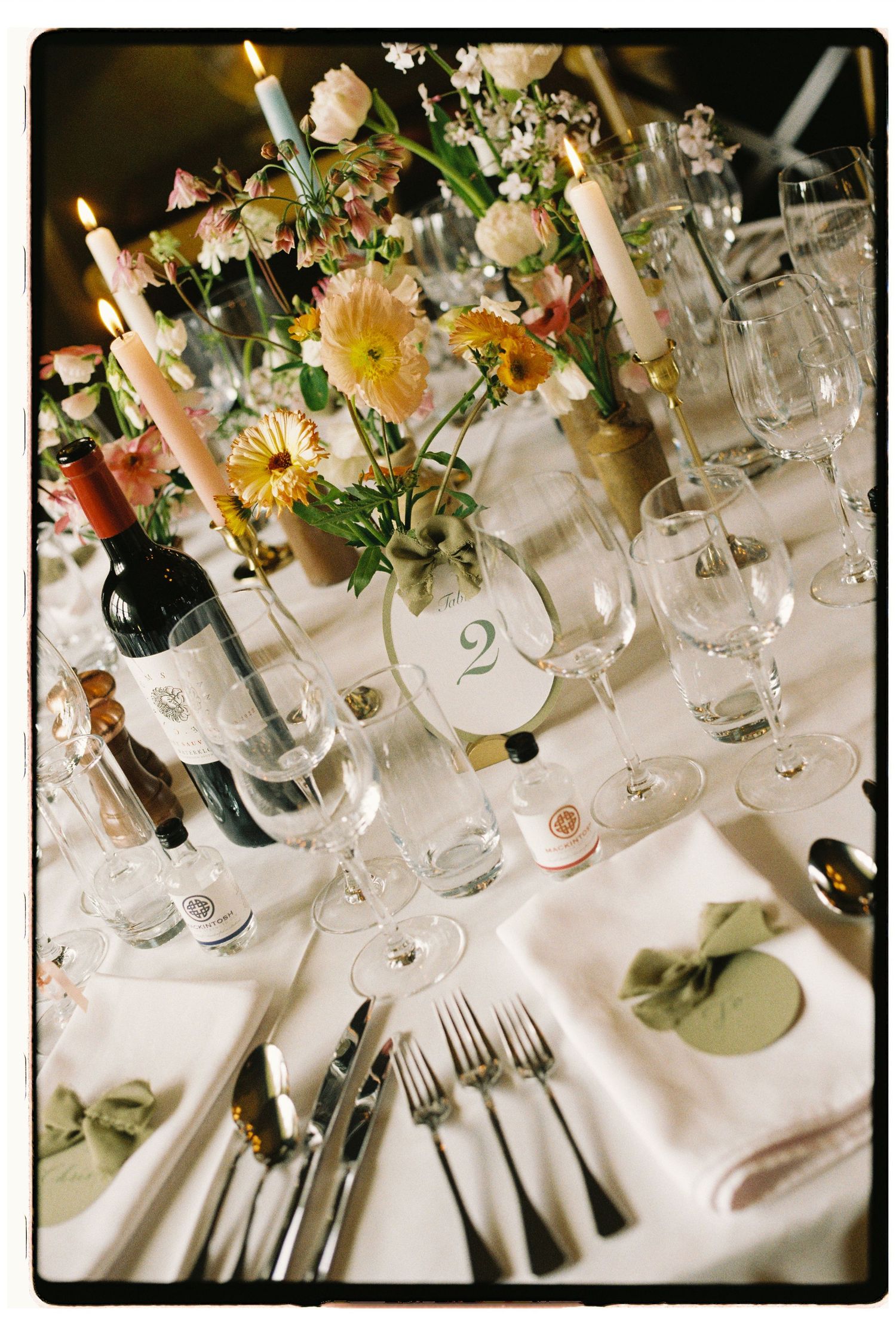 Elegant wedding table setting with floral centerpiece, candles, wine glasses, and table number 2 on white linen.
