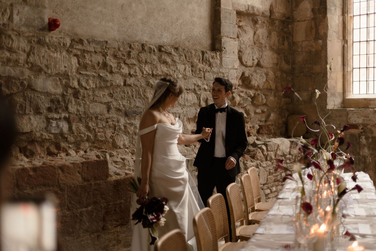 A couple shares an intimate moment in a rustic stone venue with a long candlelit dining table.