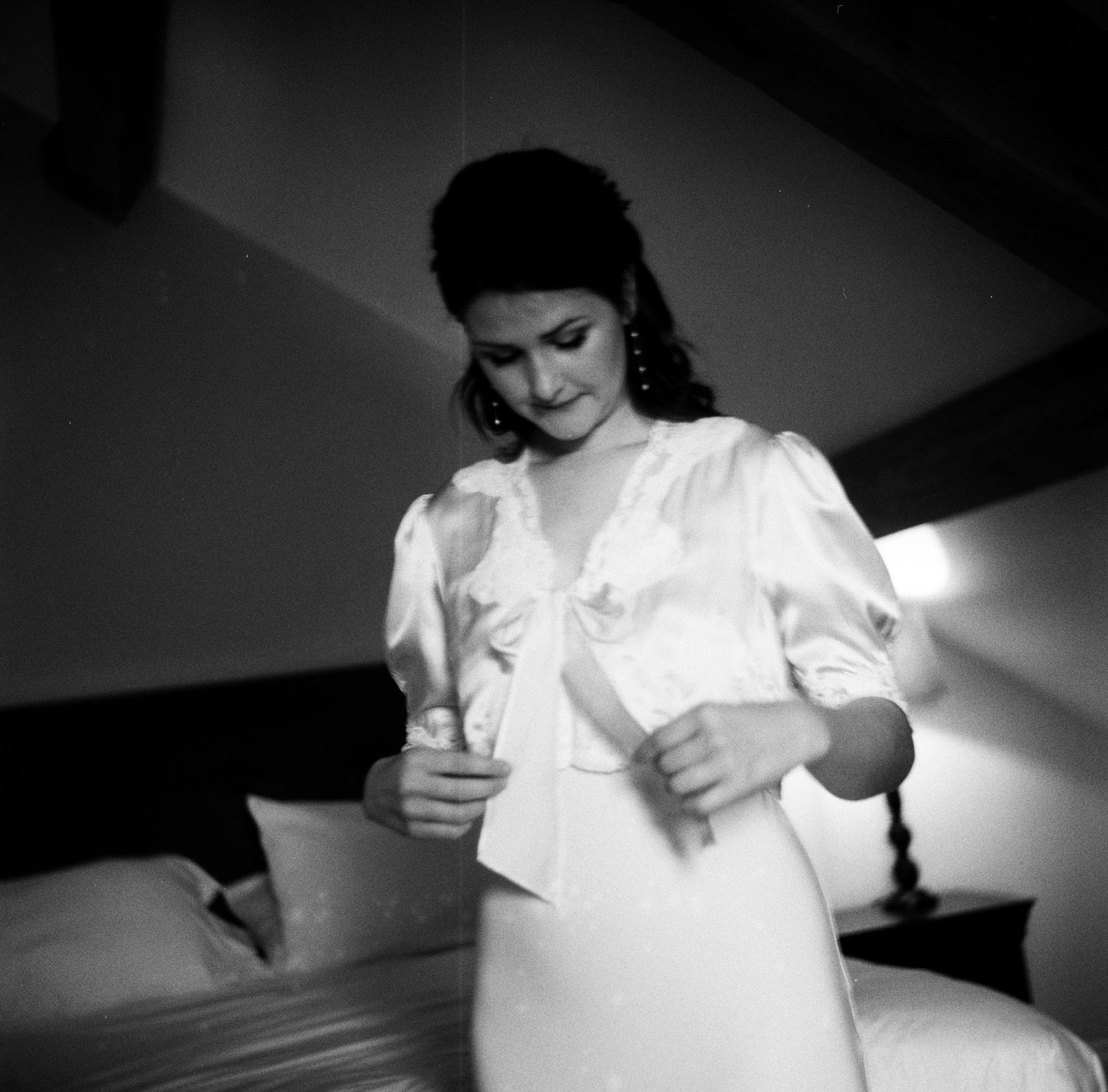A vintage black and white photograph shows a person dressed in elegant white attire in a softly lit interior setting.
