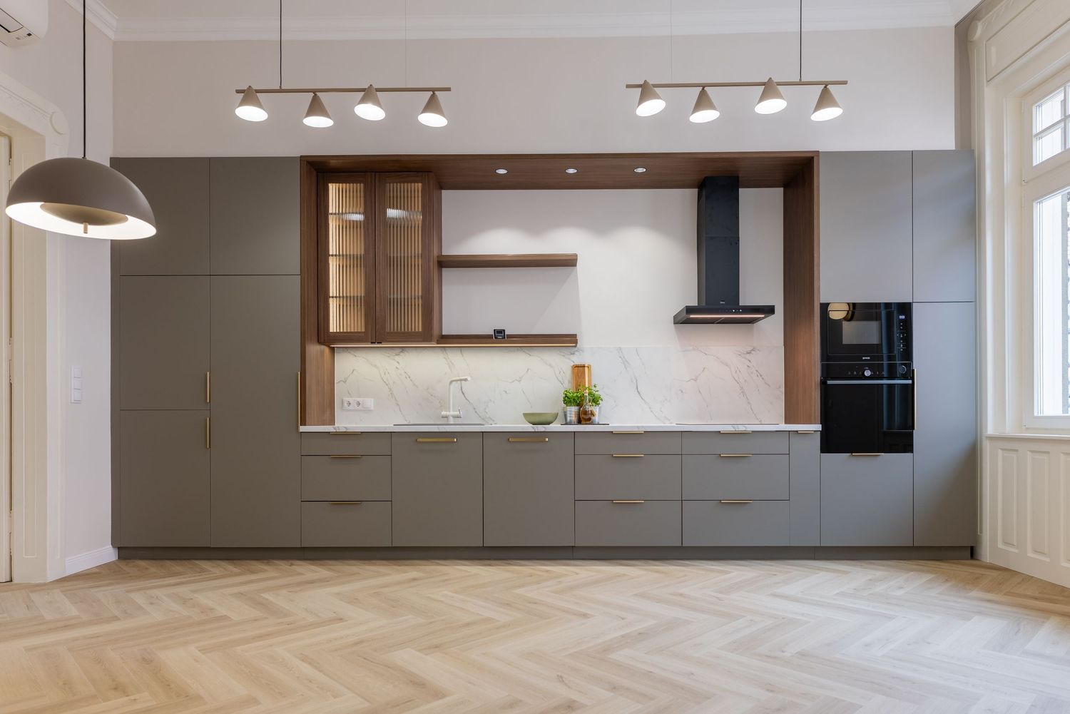 Modern kitchen with gray cabinets, marble backsplash, wood accents, and herringbone parquet floor.