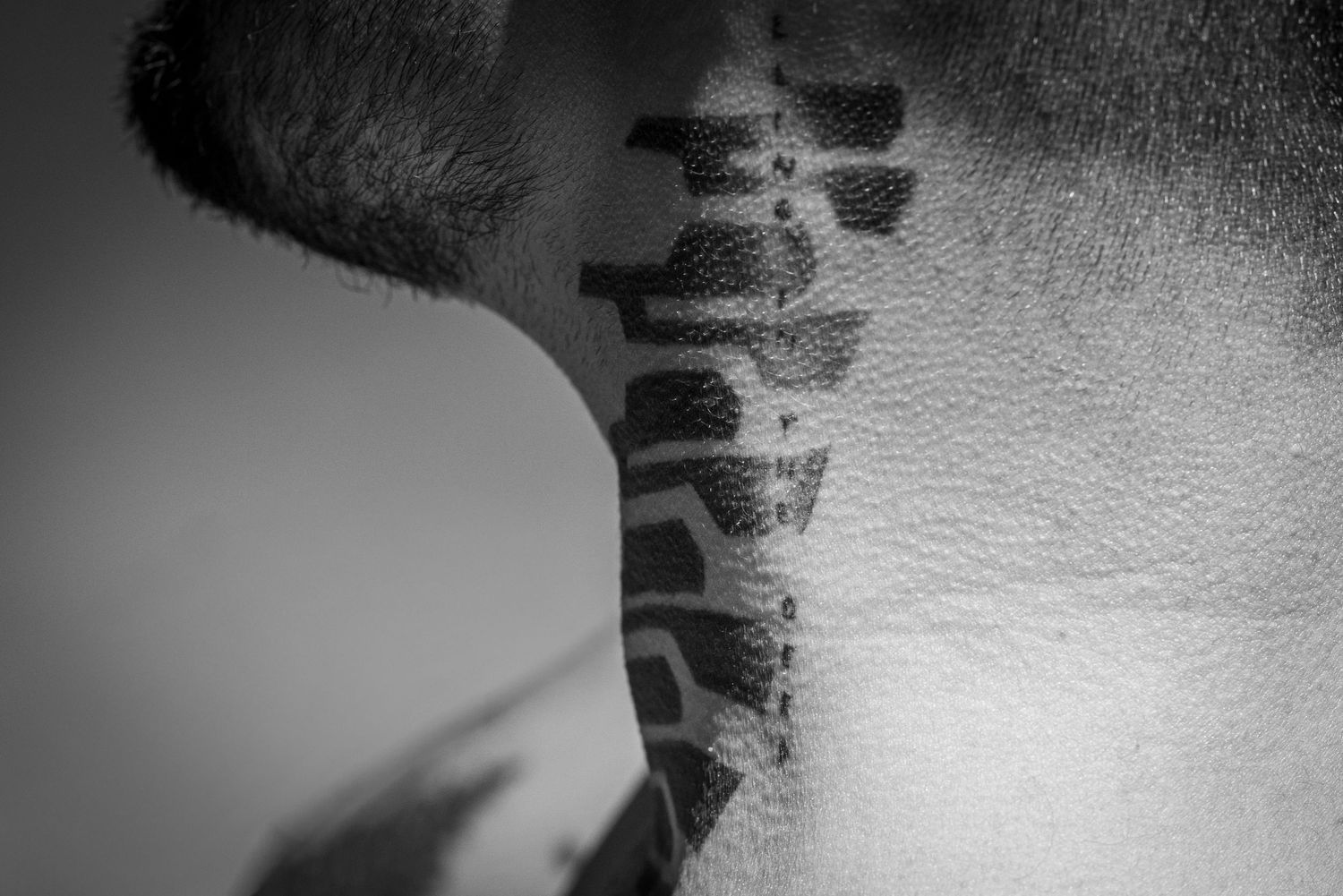 Close-up black and white photo of a spine tattoo on a mans neck.