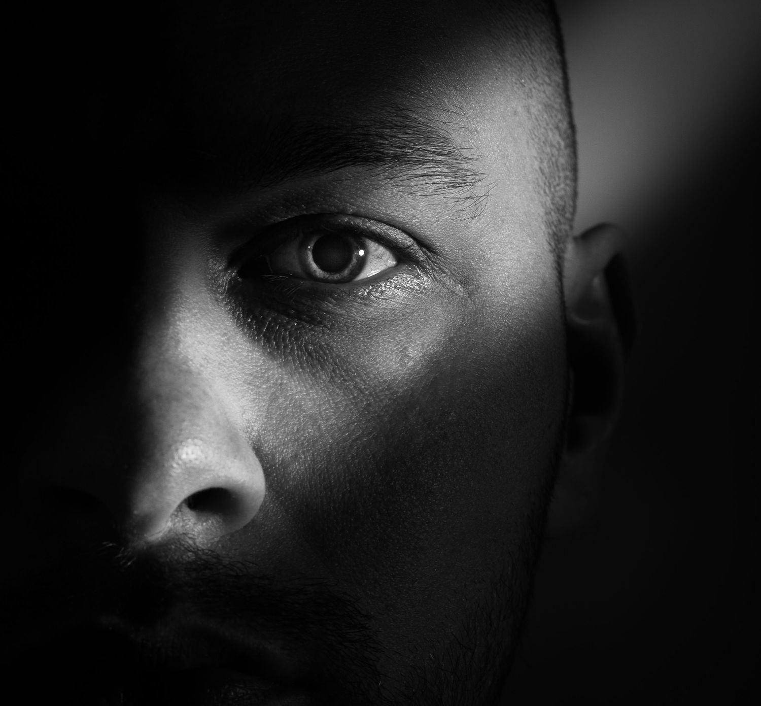 Dramatic black and white close-up portrait of a man with intense eyes and facial stubble.