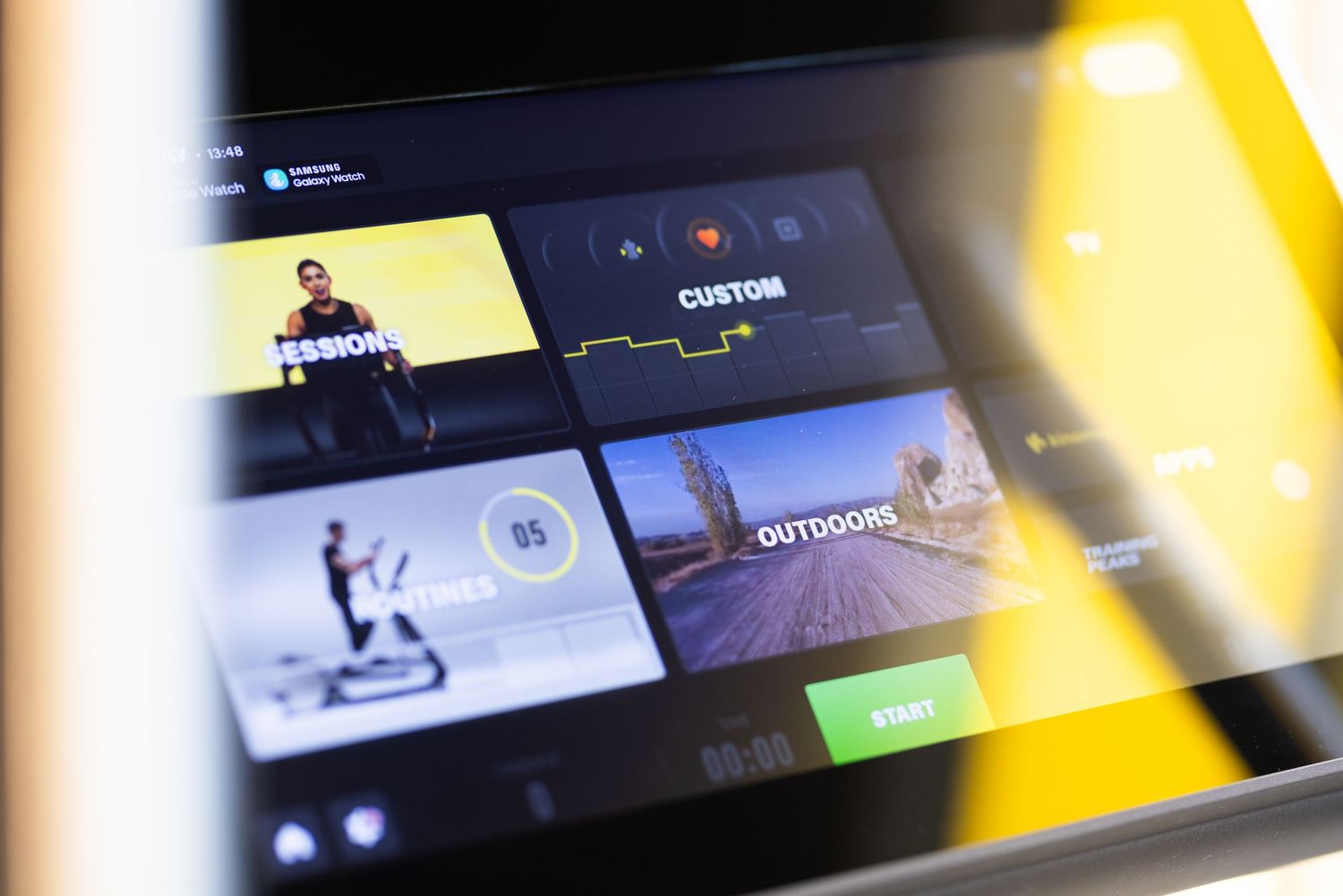 Fitness equipment touchscreen displaying workout sessions including custom, outdoors, and training program options.