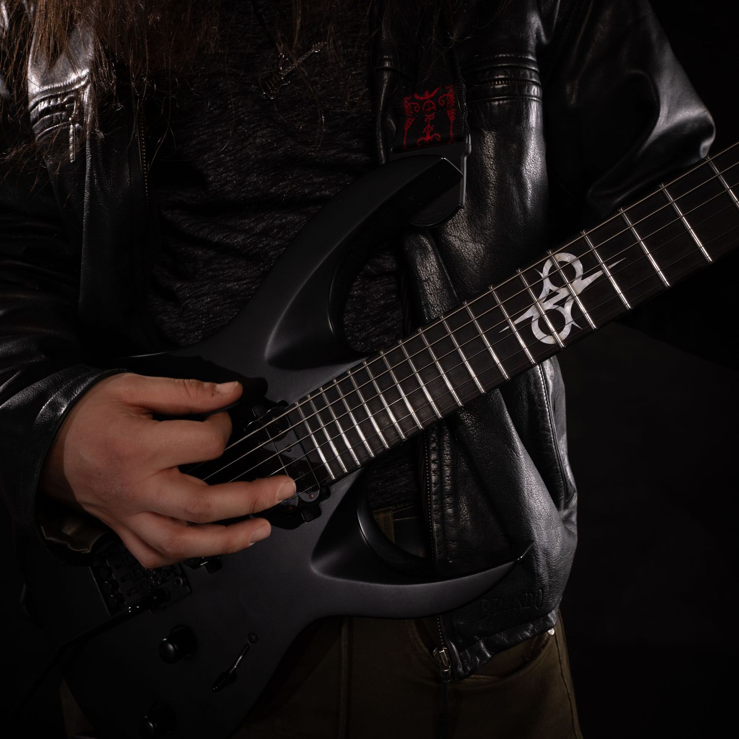 Metal guitarist in black leather jacket holding dark electric guitar in studio.