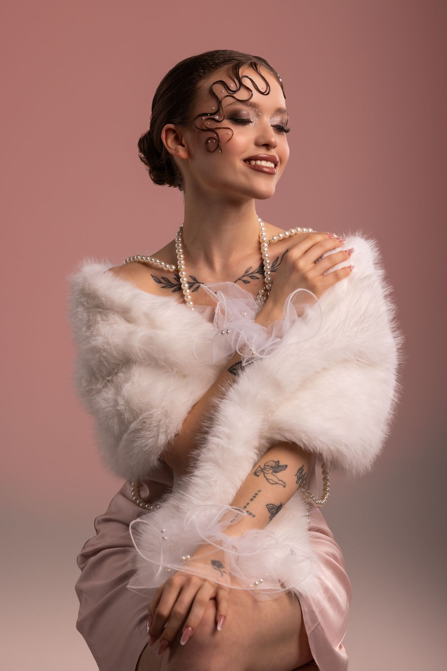 Smiling tattooed woman in white fur wrap and pearl necklace with artistic snake face paint on pink background.