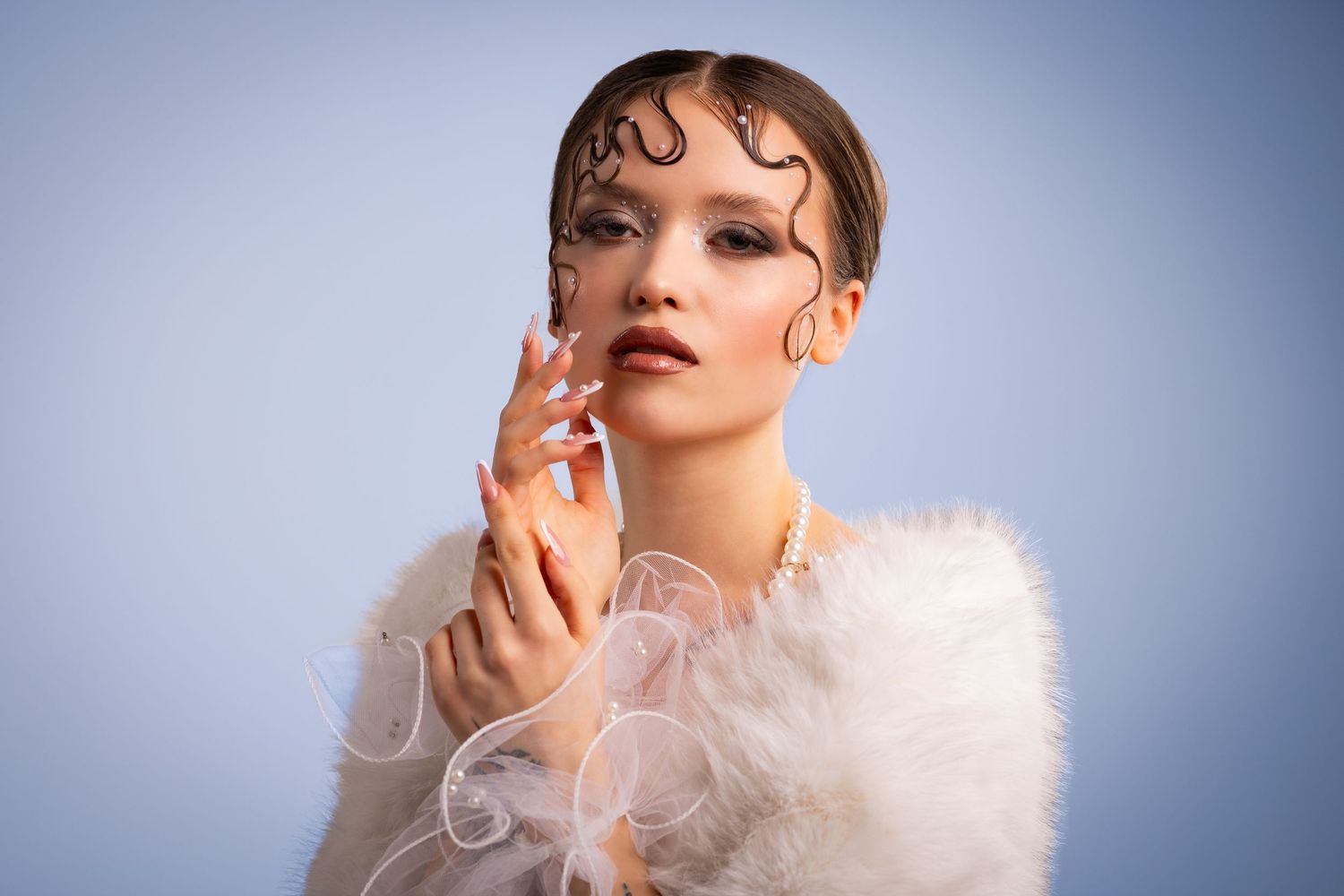 Fashion model with wet hair styling and white feather wrap posing against a soft blue studio background.