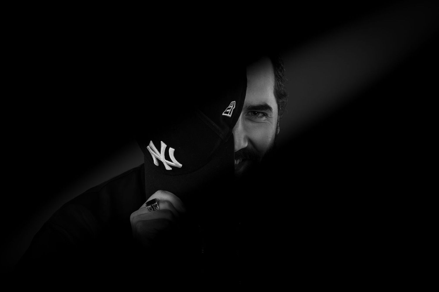 Dramatic black and white portrait of man wearing NY Yankees cap emerging from shadows.