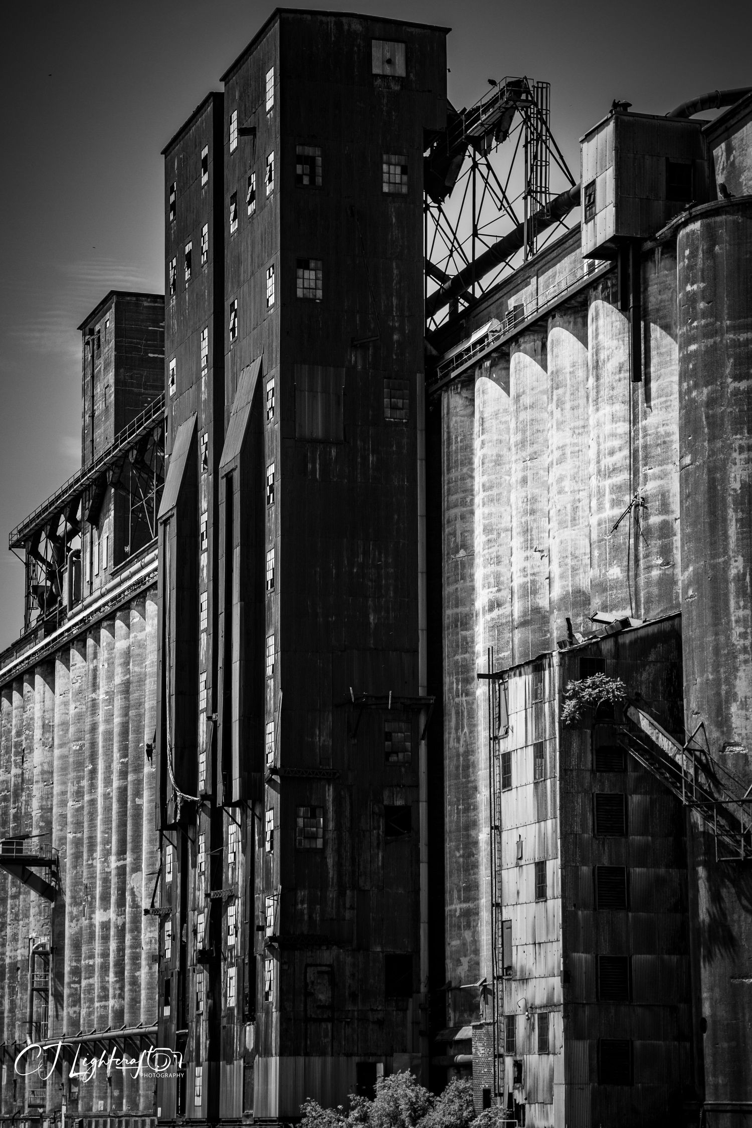 Black and white photo of massive industrial grain silos and historic mill buildings with metal framework.
