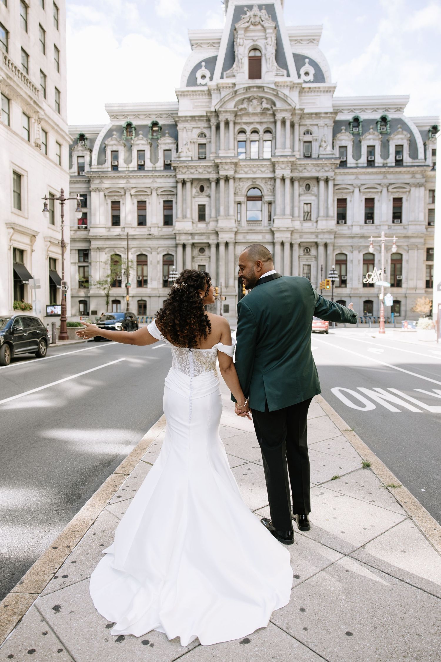 Bride and groom holding hands in front of grand historic city hall building.