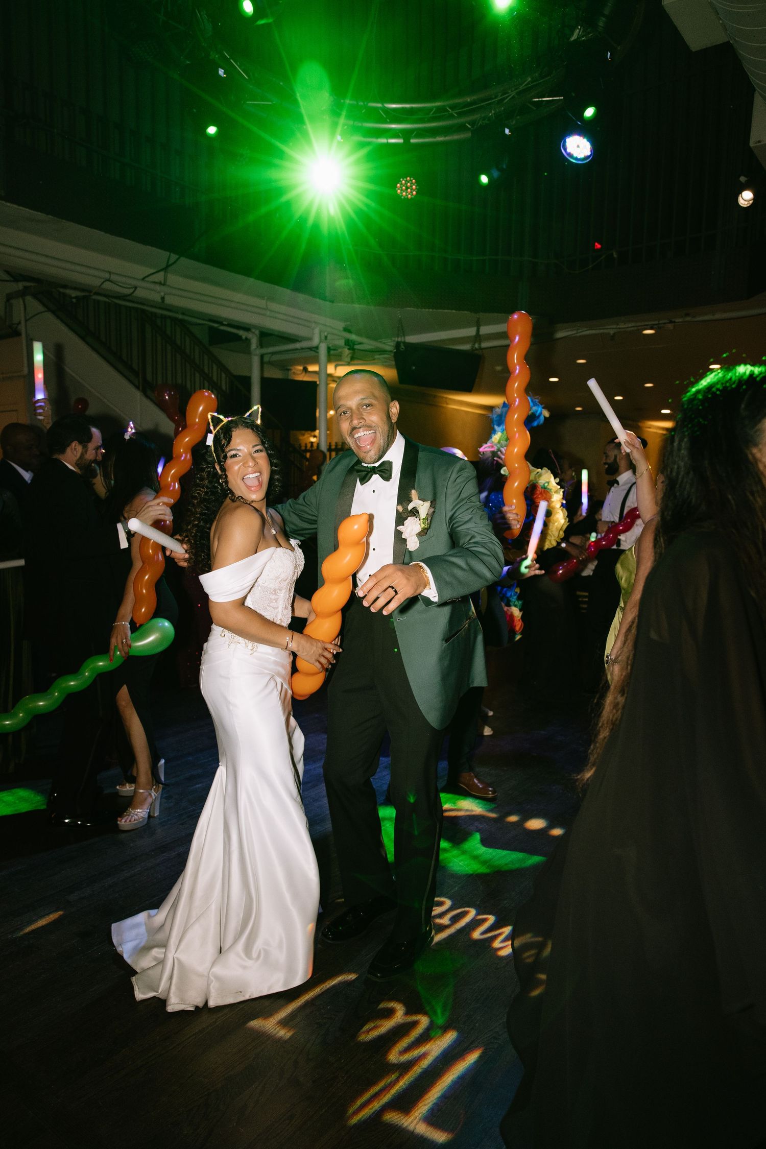 Bride and groom dancing with balloon animals under green lights at wedding reception.