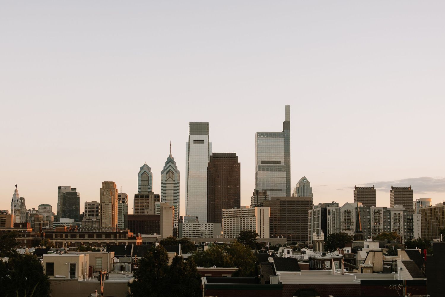 Philadelphia city skyline at dusk with iconic skyscrapers and urban rooftops against a soft evening sky.