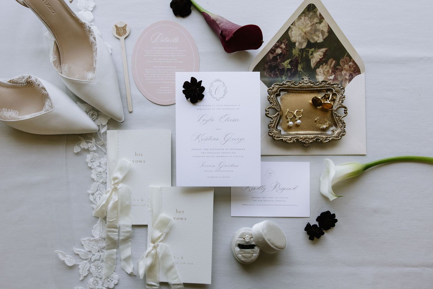 Elegant wedding stationery flat lay with floral envelope liner, white invitations, black accents, calla lily, and bridal heels.