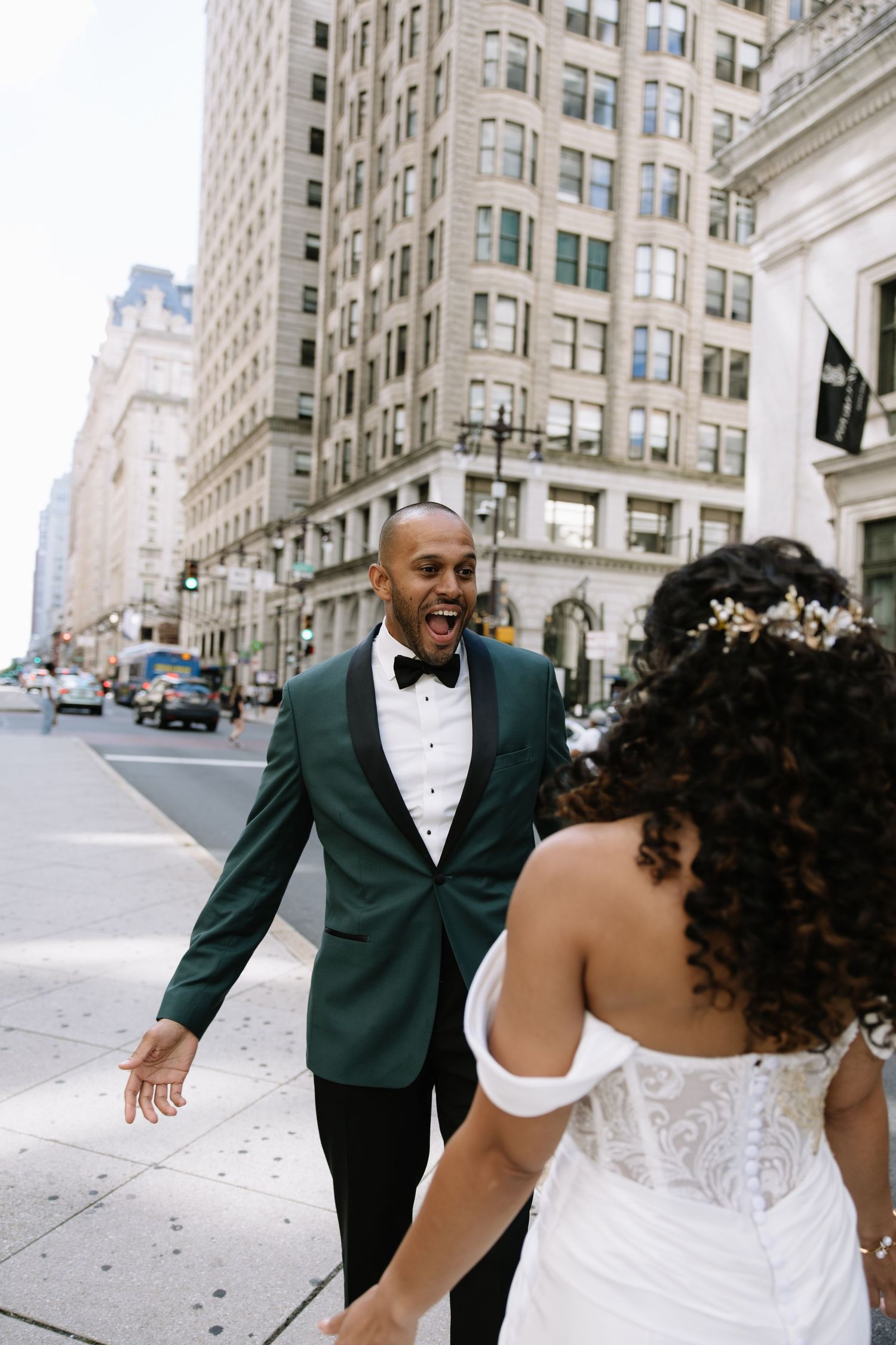 Groom in green tuxedo reacts with joy seeing bride on urban city street.