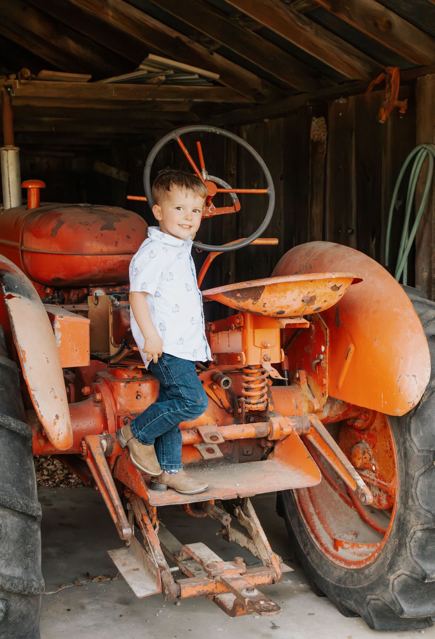 Young boy posing next to a tractor in a farm setting in rural Missouri, Olney, MO, during family session