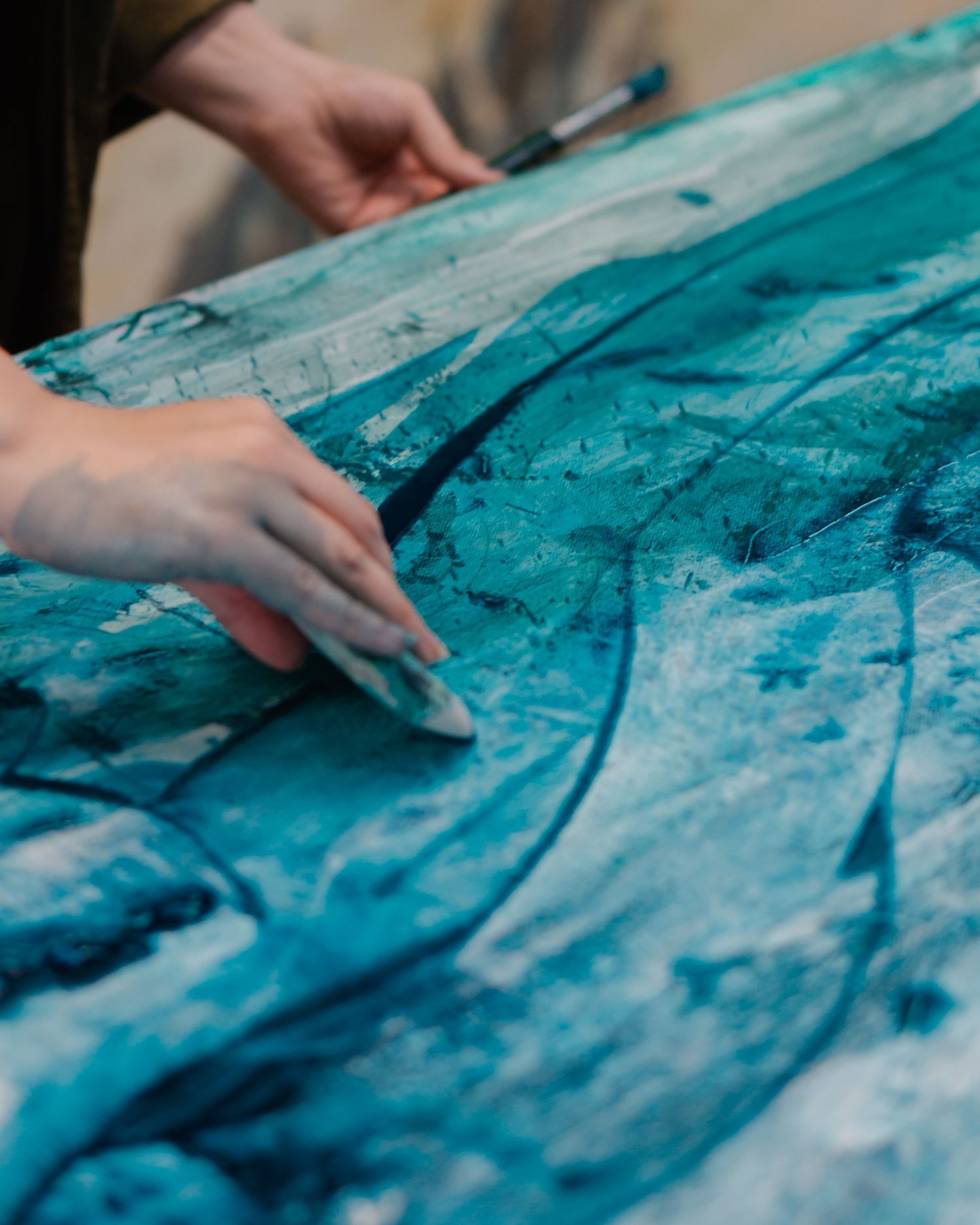 Artist hands spreading teal and blue paint across a large canvas in an abstract painting process.
