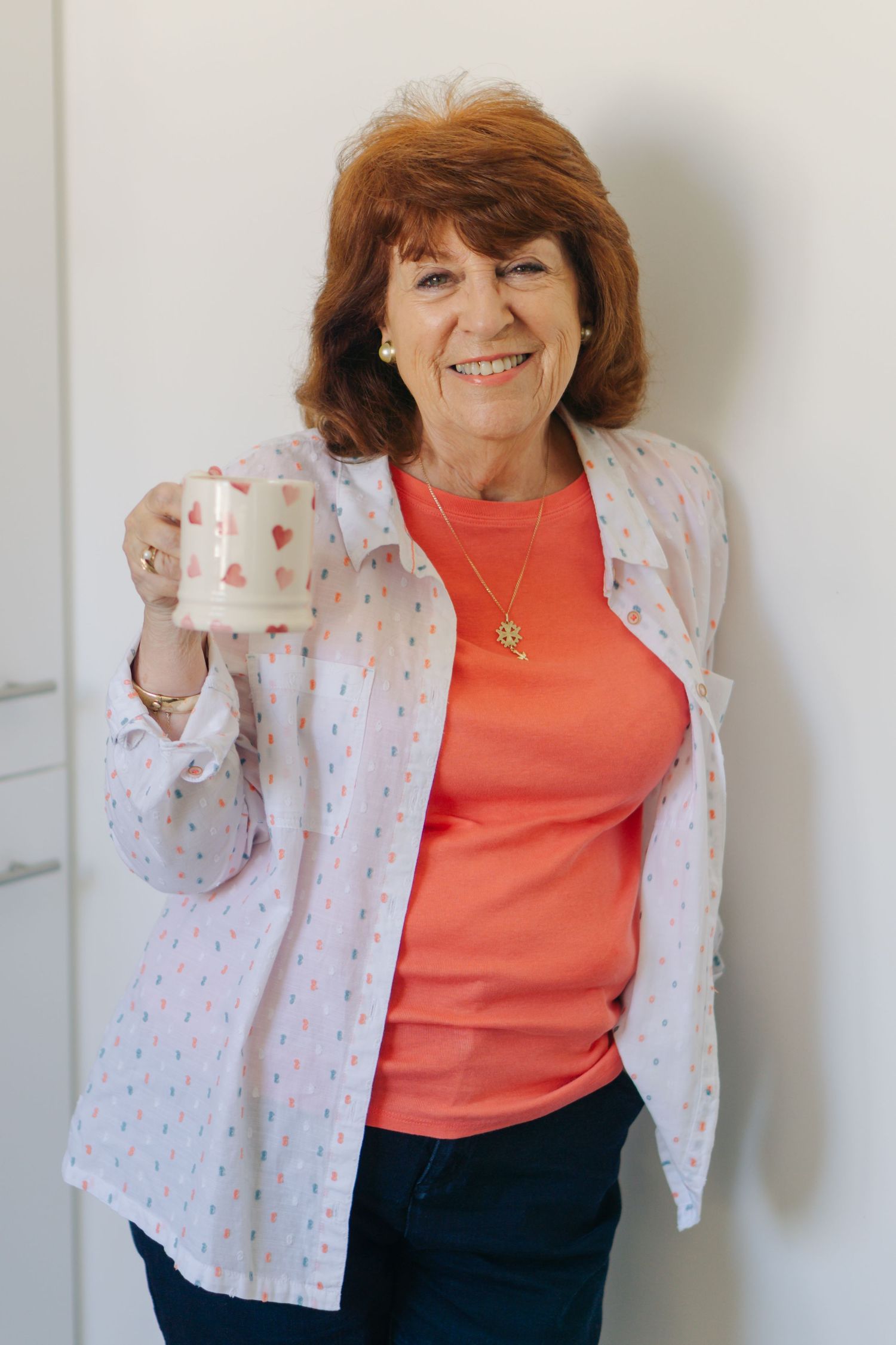 Plymouth based therapist, Grace Chatting, in red top and pink shirt holding a decorative mug, leaning against a white wall.