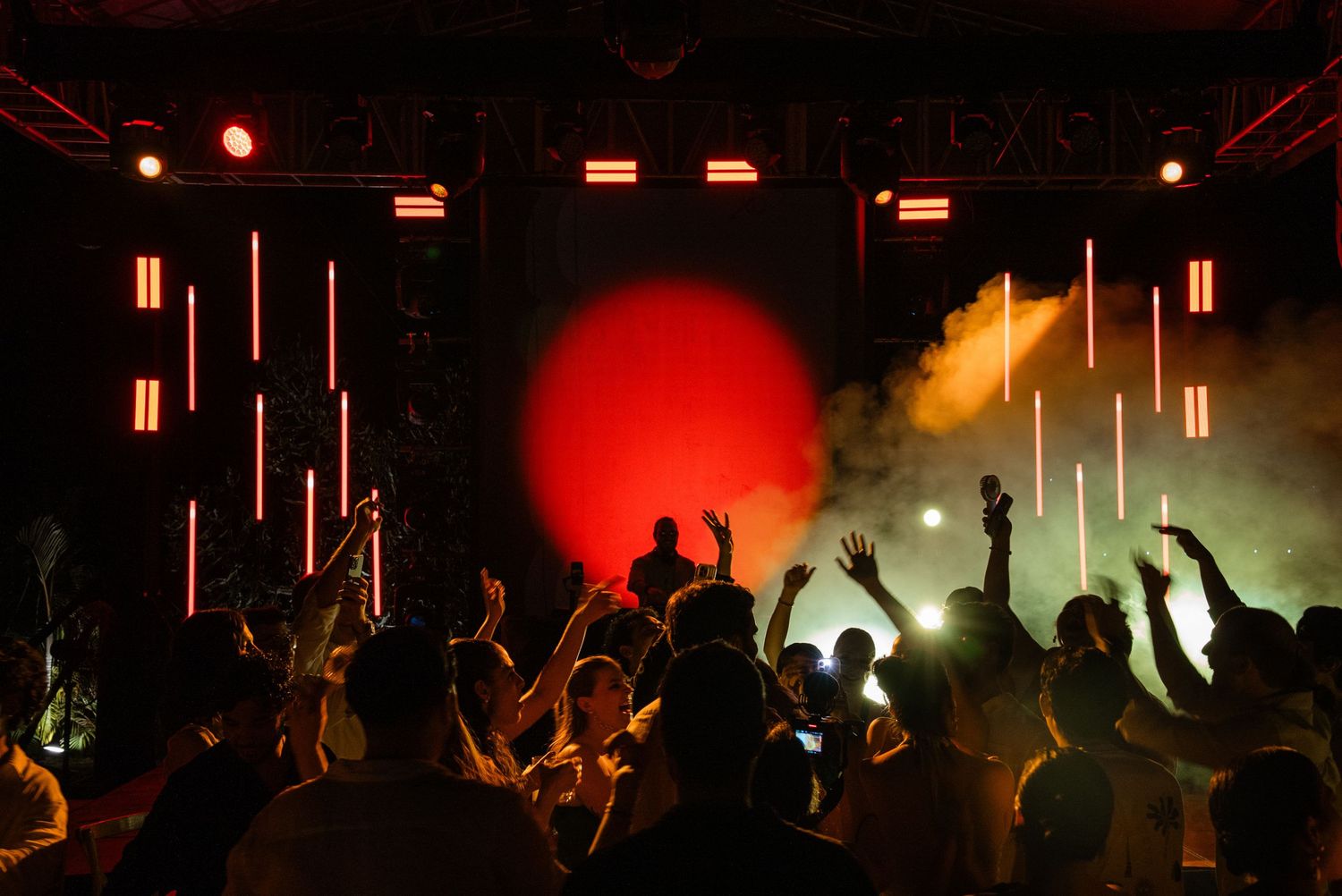 Energetic wedding reception crowd dancing under vibrant red and green stage lights with smoke effects.