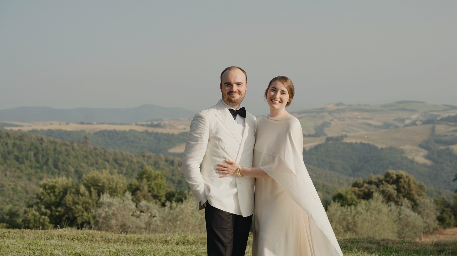 Bride and groom posing together in Tuscan countryside landscape on their wedding day.