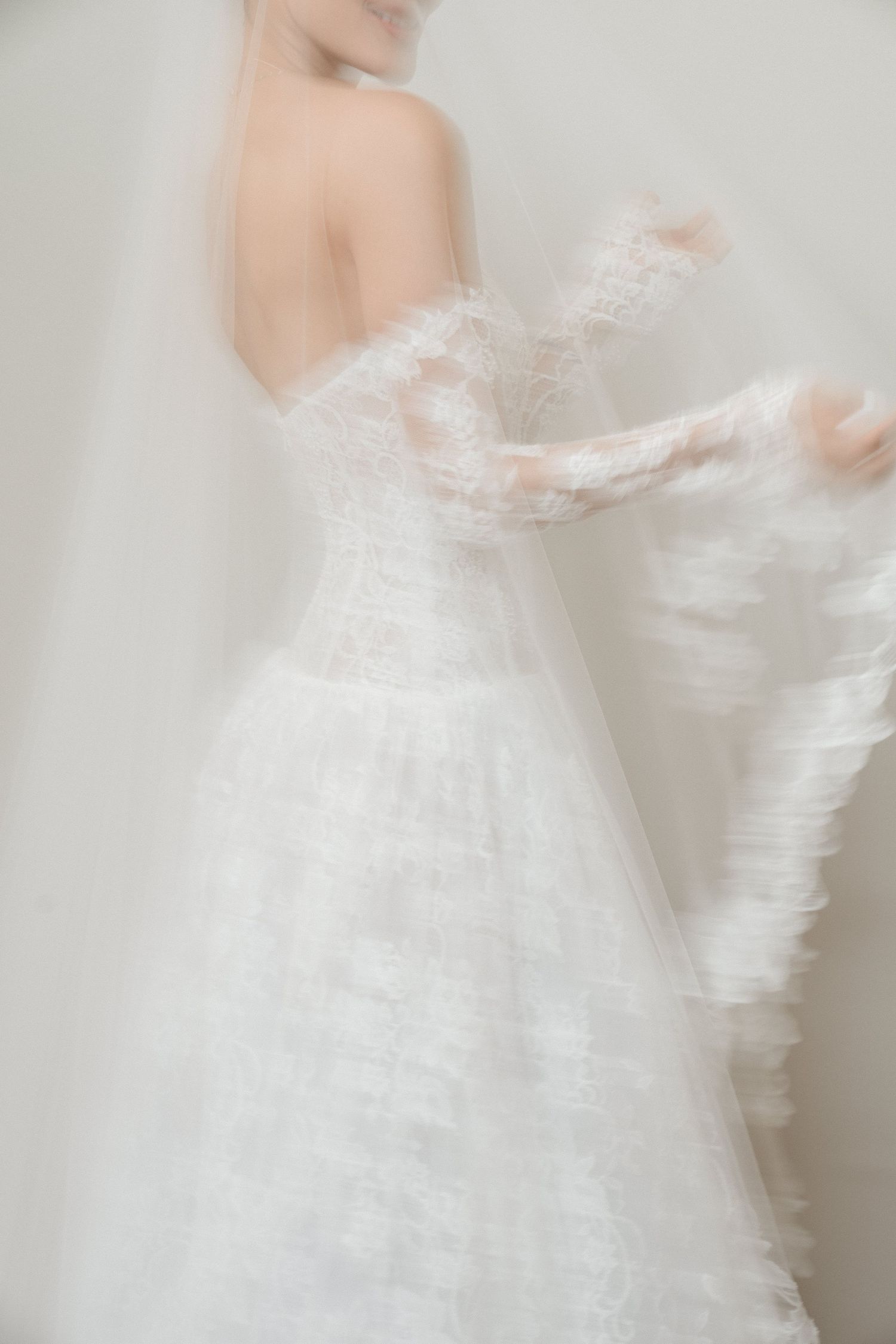 Artistic motion blur of bride in off-shoulder lace gown holding her veil.