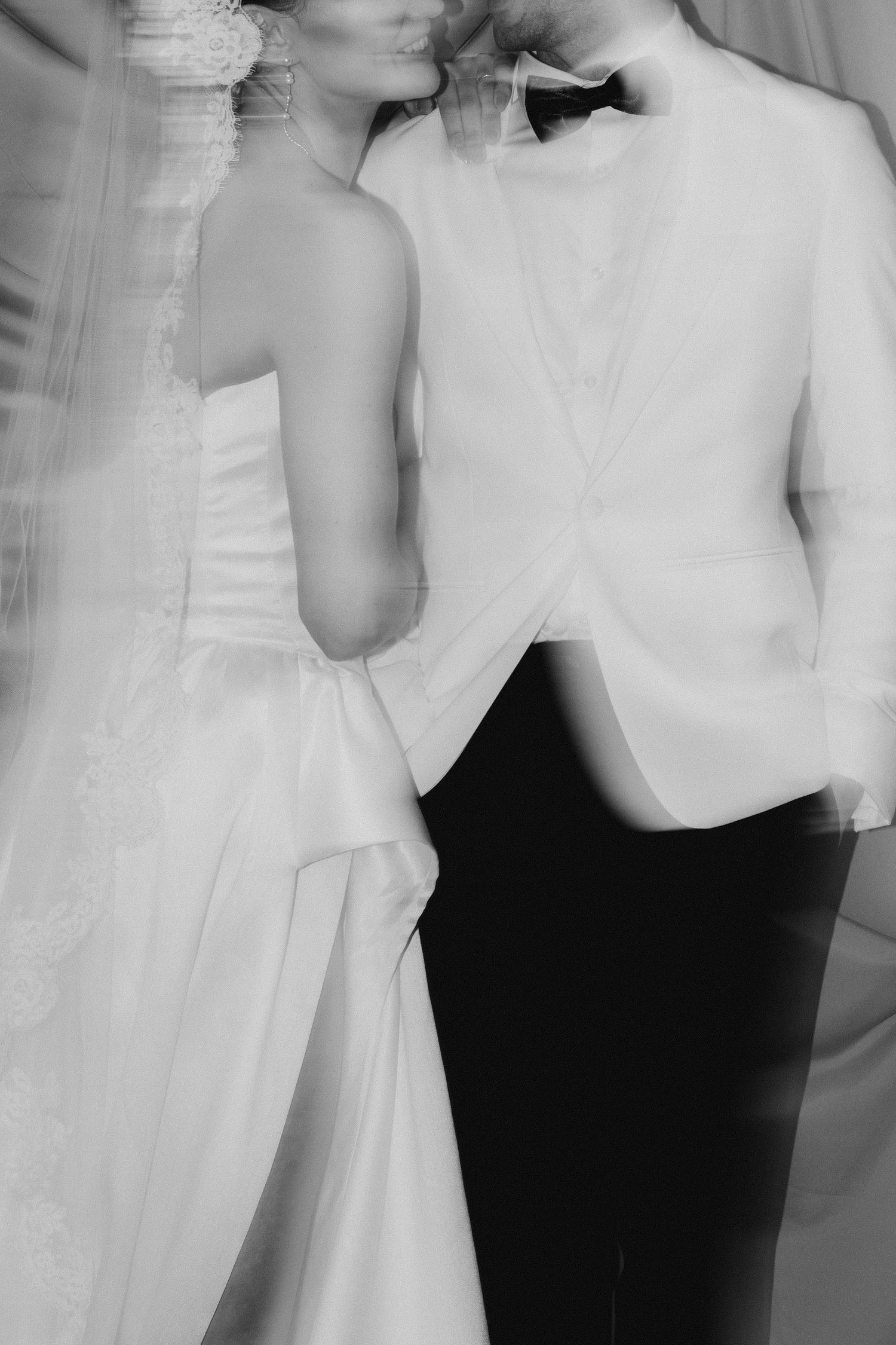 Black and white motion blur photo of bride in strapless gown and groom in white tuxedo holding hands.