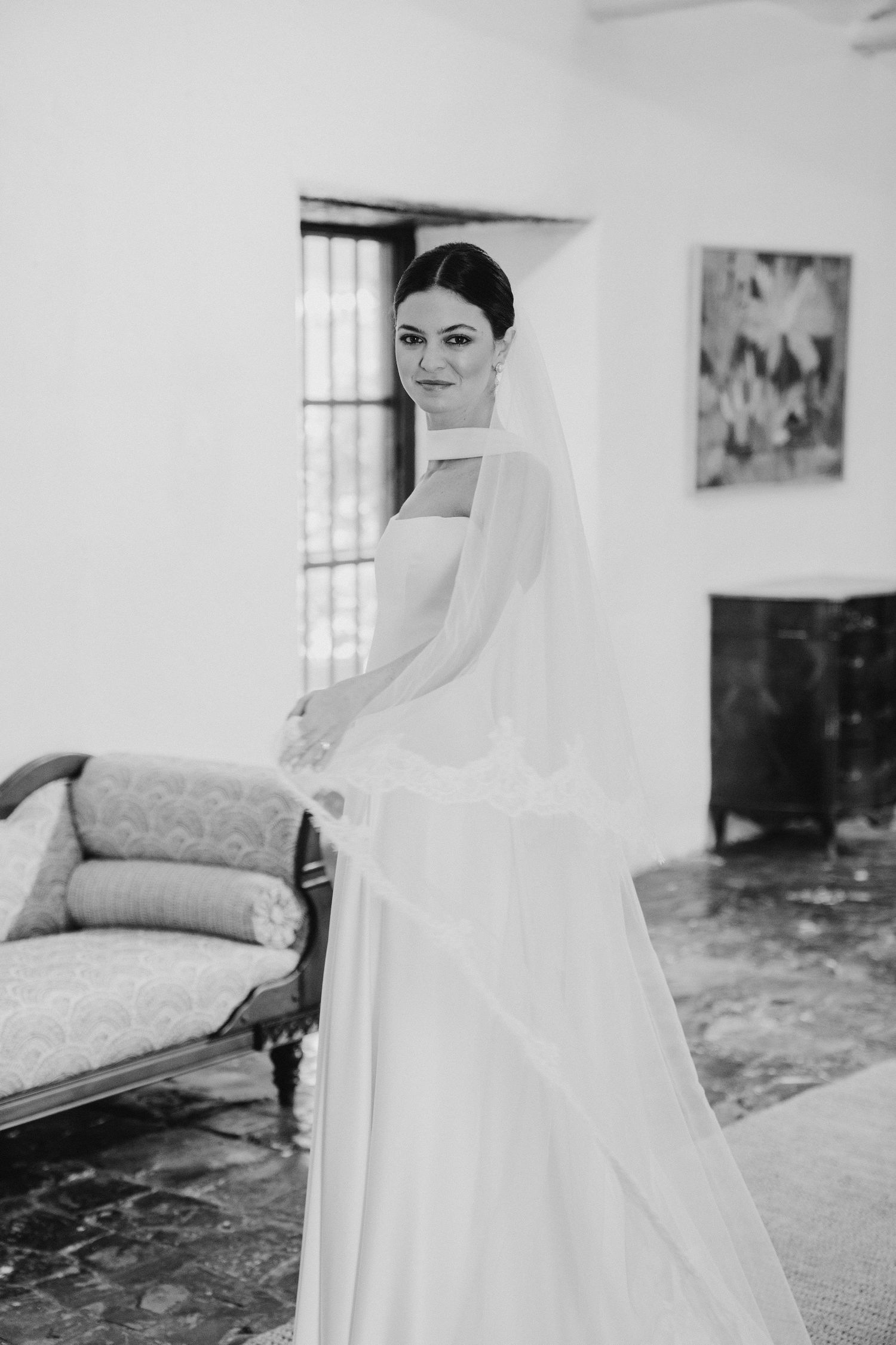 Elegant bride in white gown and veil posing in a classic interior room.
