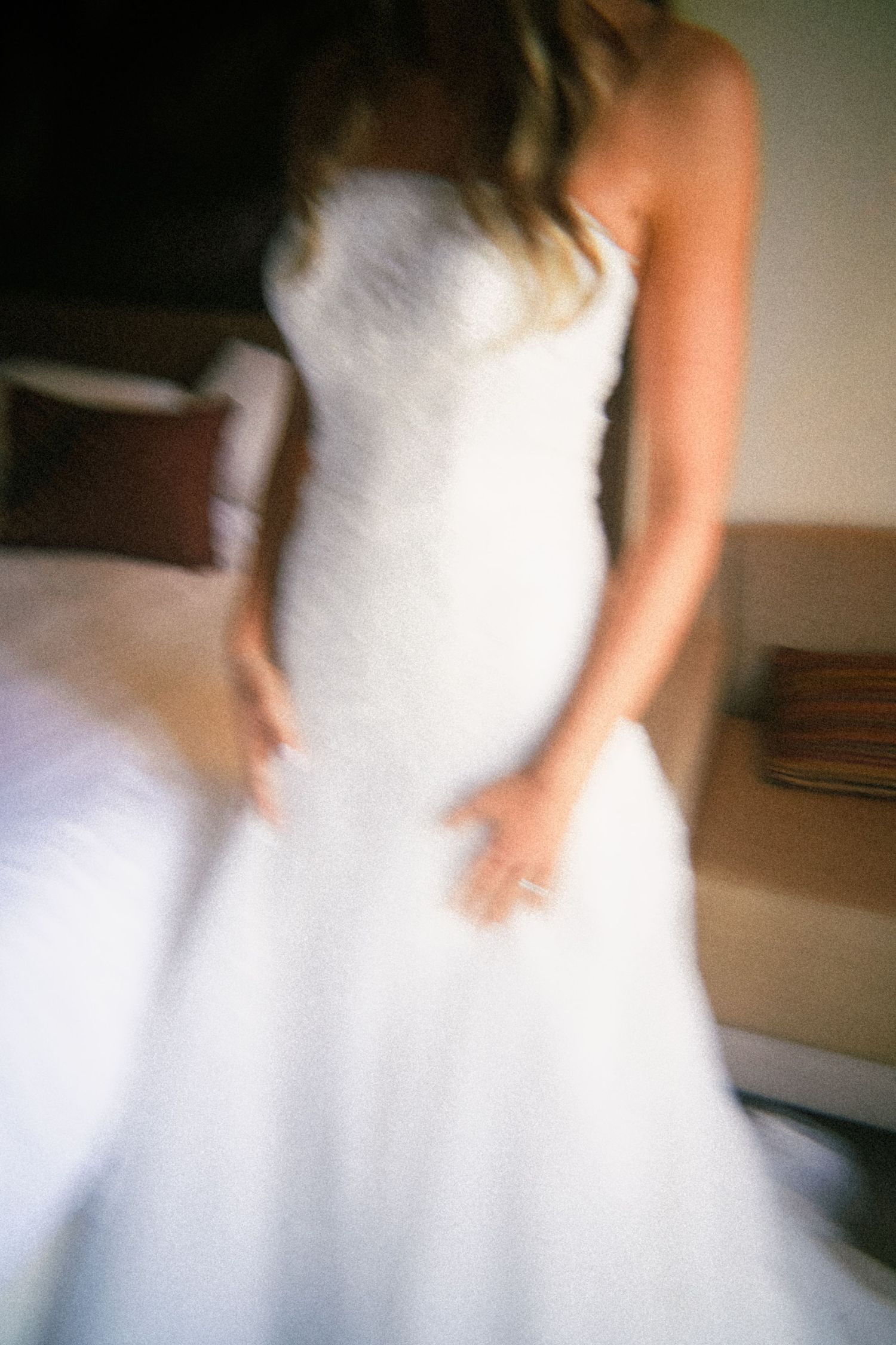 Blurred artistic photo of a bride in a white strapless wedding gown holding her dress in a hotel room.
