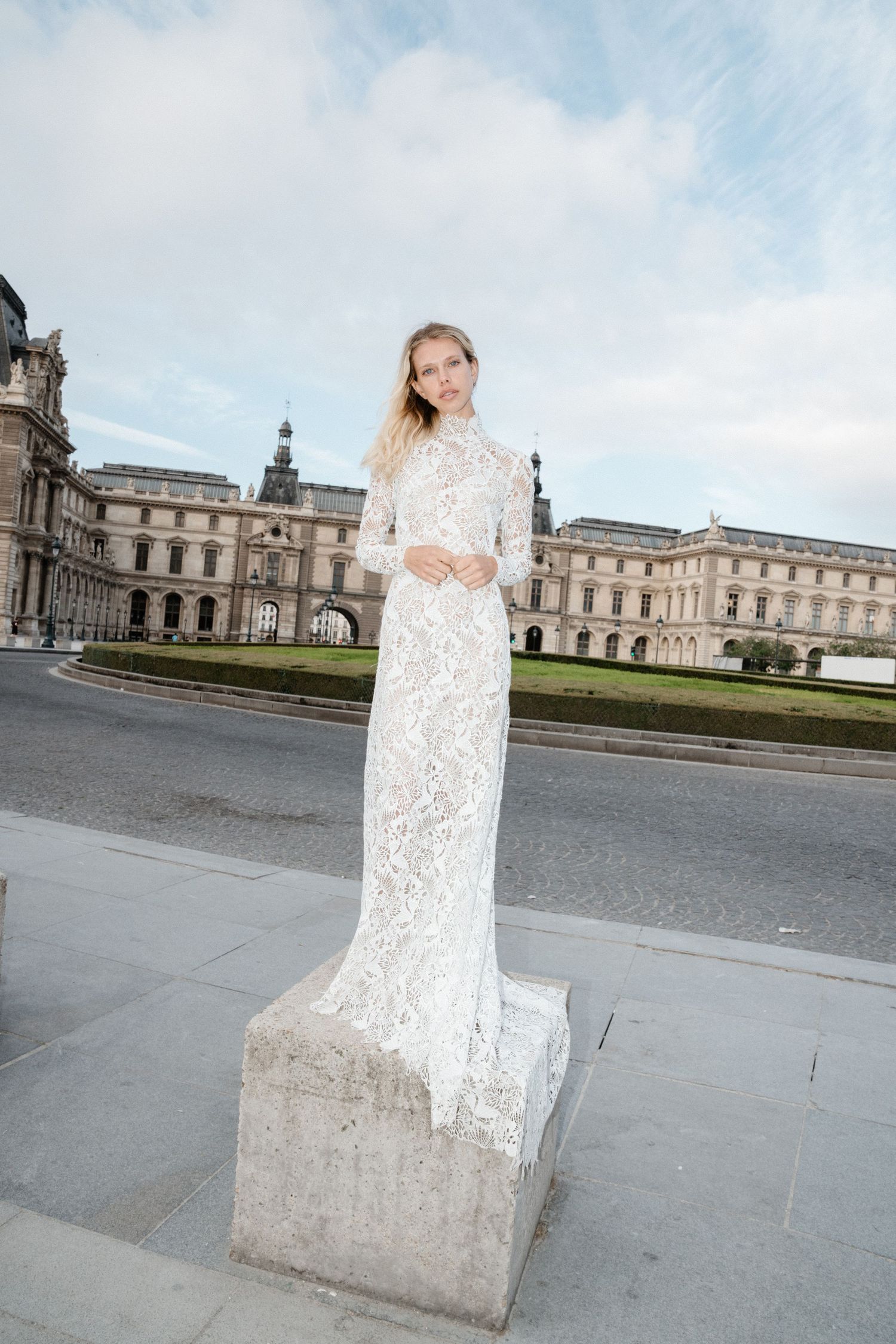 Bride in an elegant long-sleeve lace wedding dress standing on steps with a classical European building backdrop.