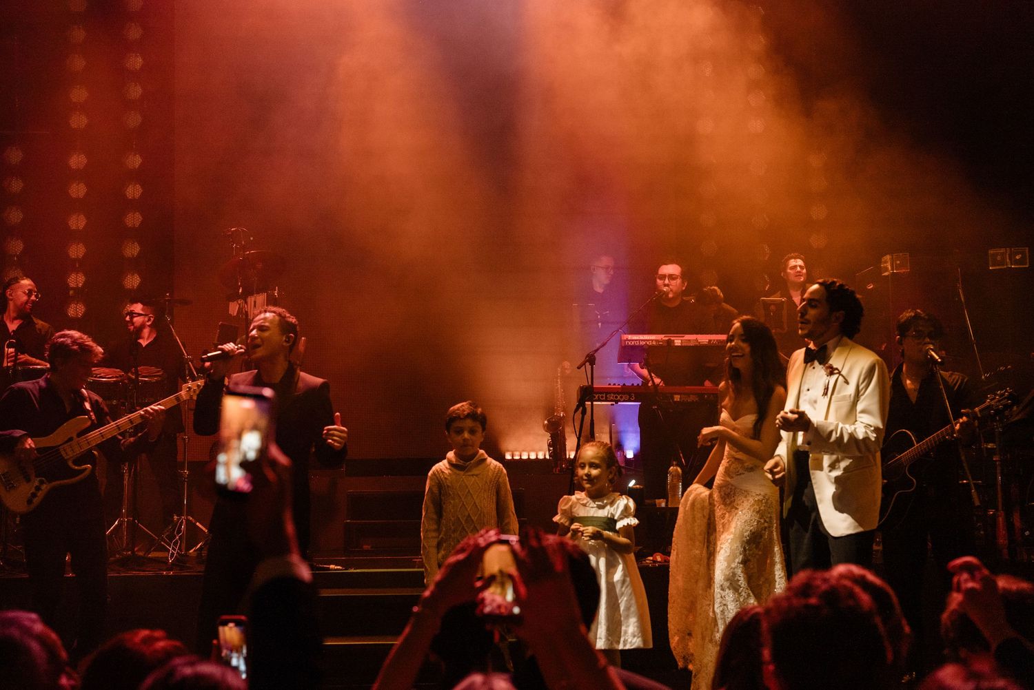 Wedding band performing on stage with dramatic orange lighting and smoke at a reception party.