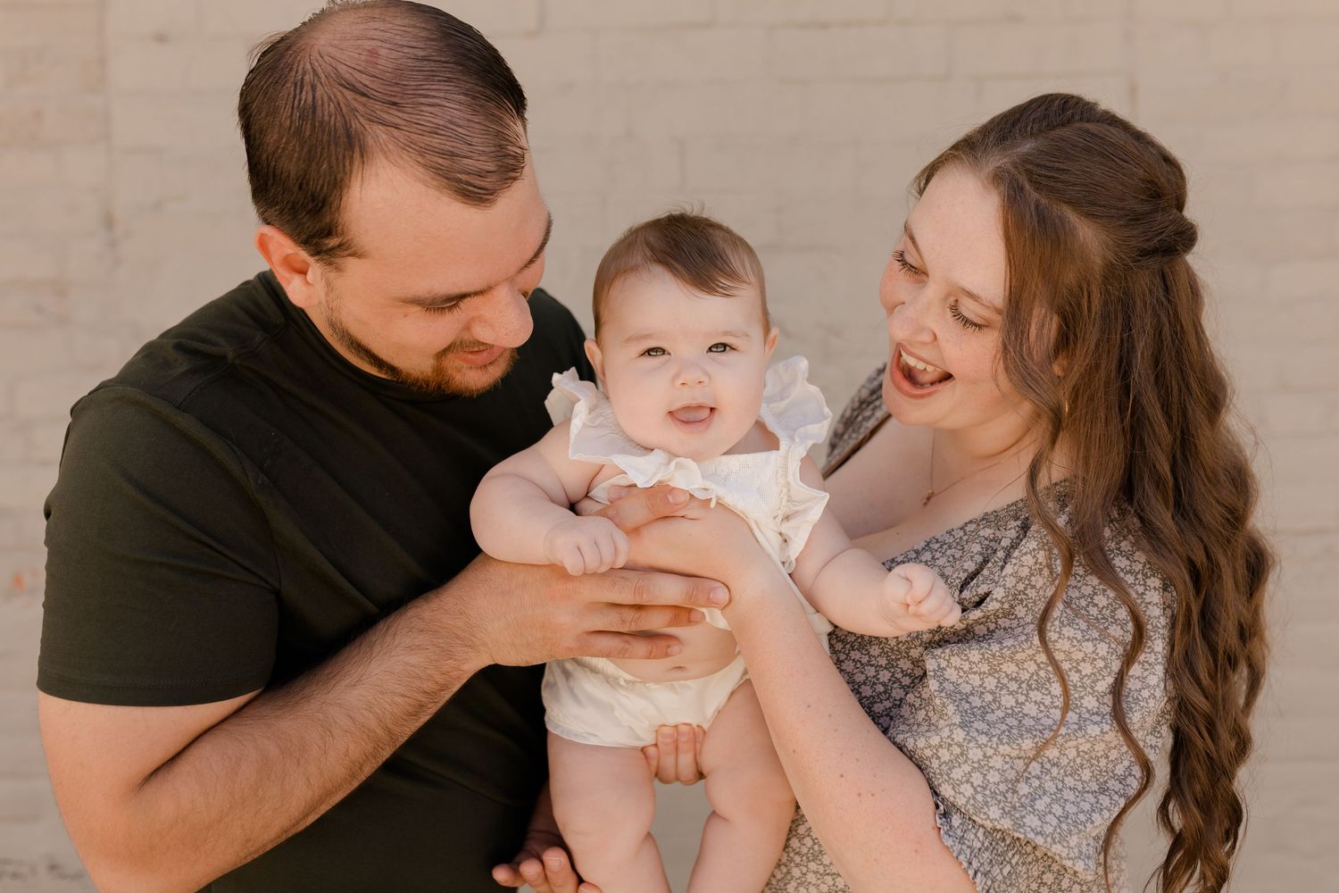 A loving family portrait with parents holding their smiling baby in a warm downtown setting.