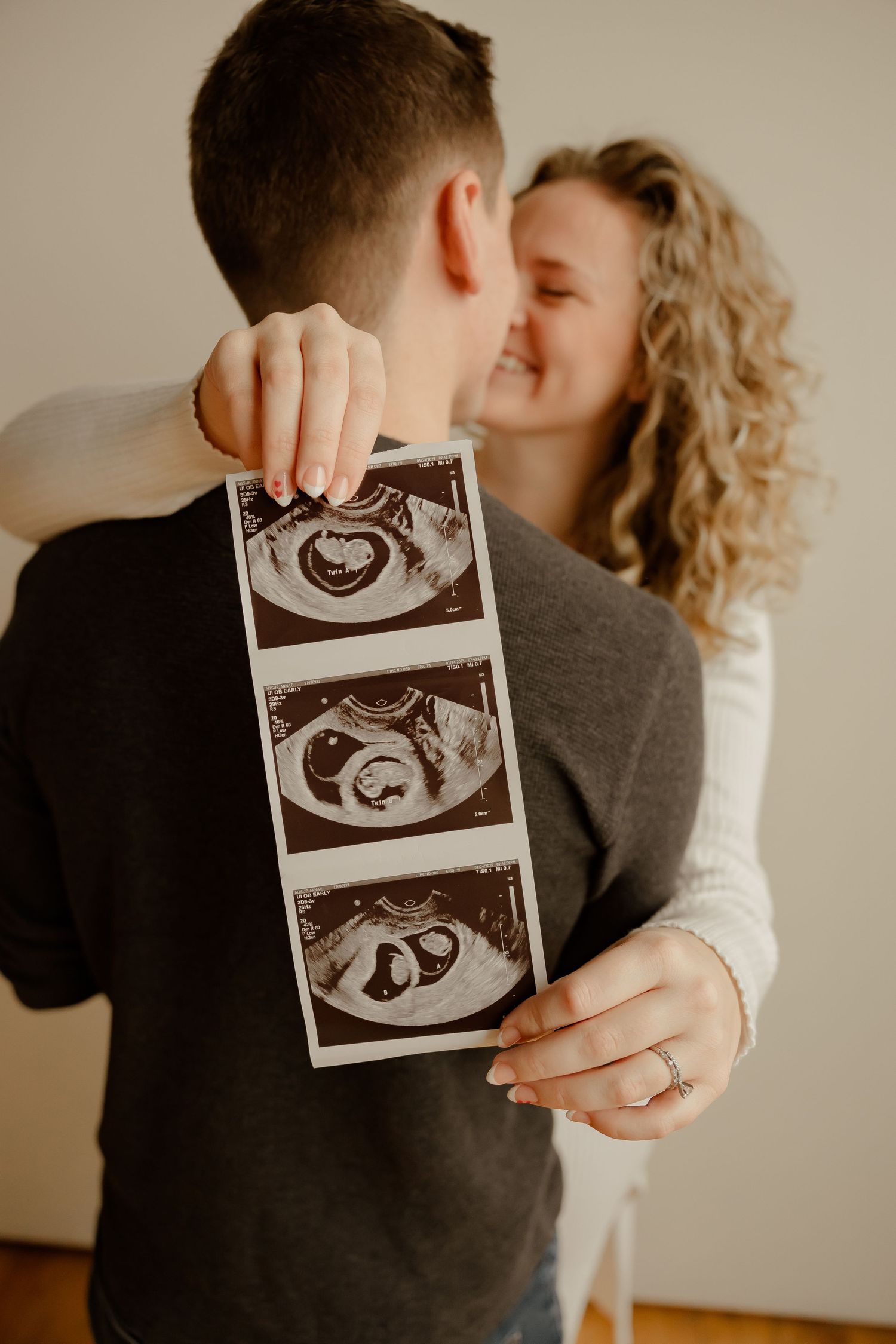 A couple shares a tender moment while holding ultrasound images showing three stages of their baby's development.