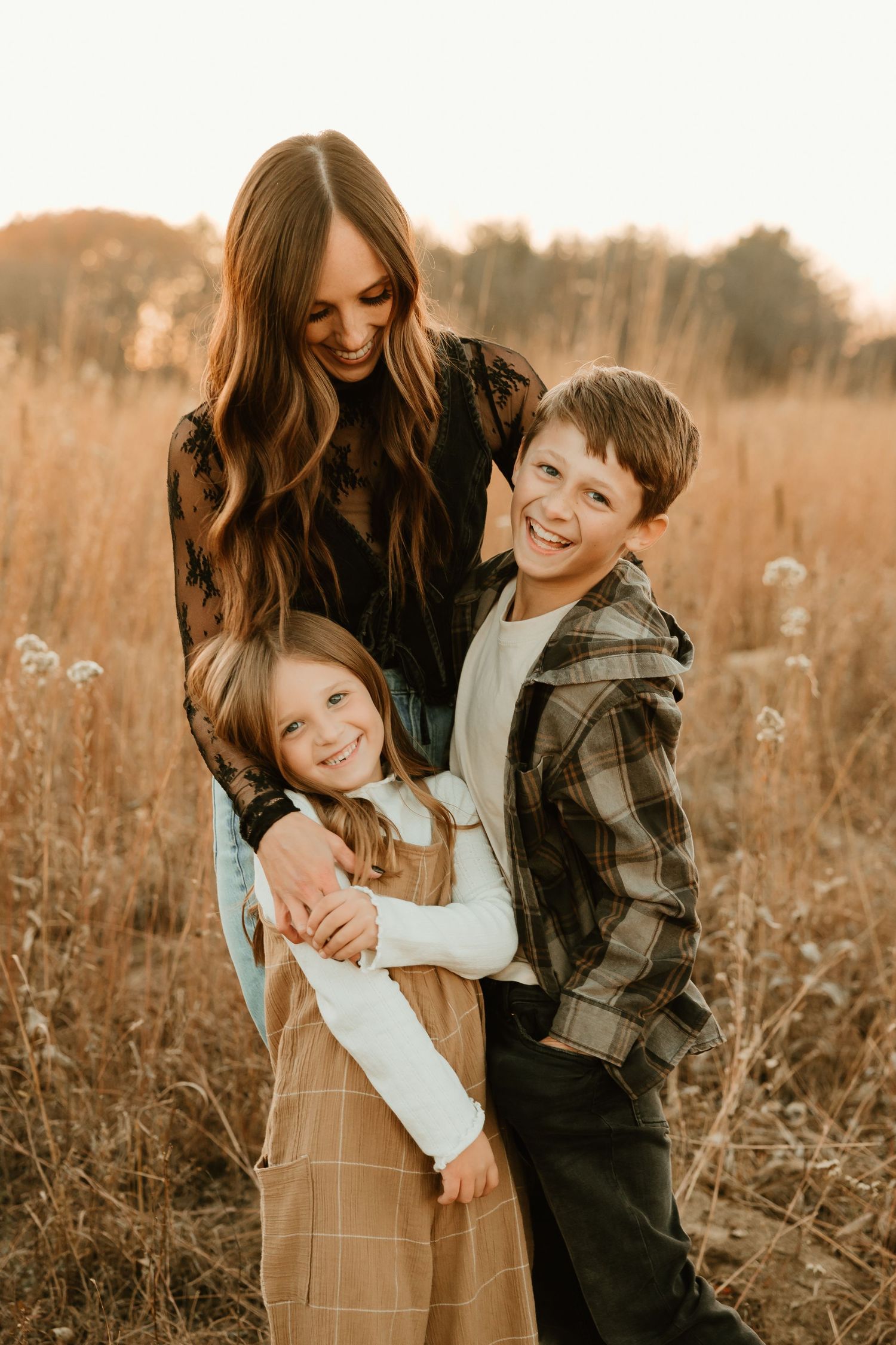 A family shares warm embraces and laughter while standing together in a golden autumn field during sunset.