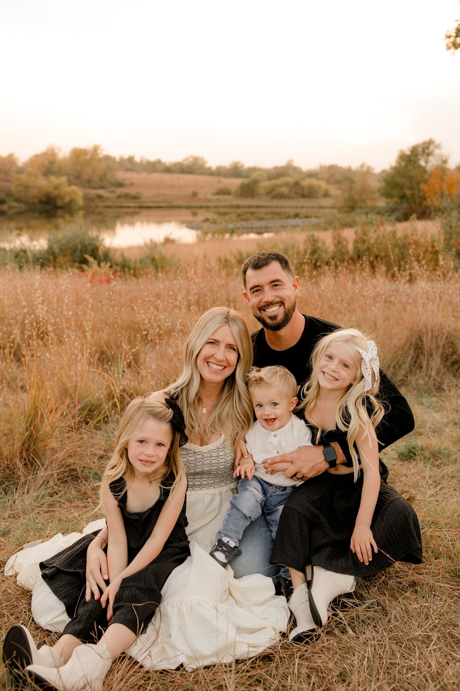 Beautiful autumn family portrait taken in a golden field at sunset near a serene pond.