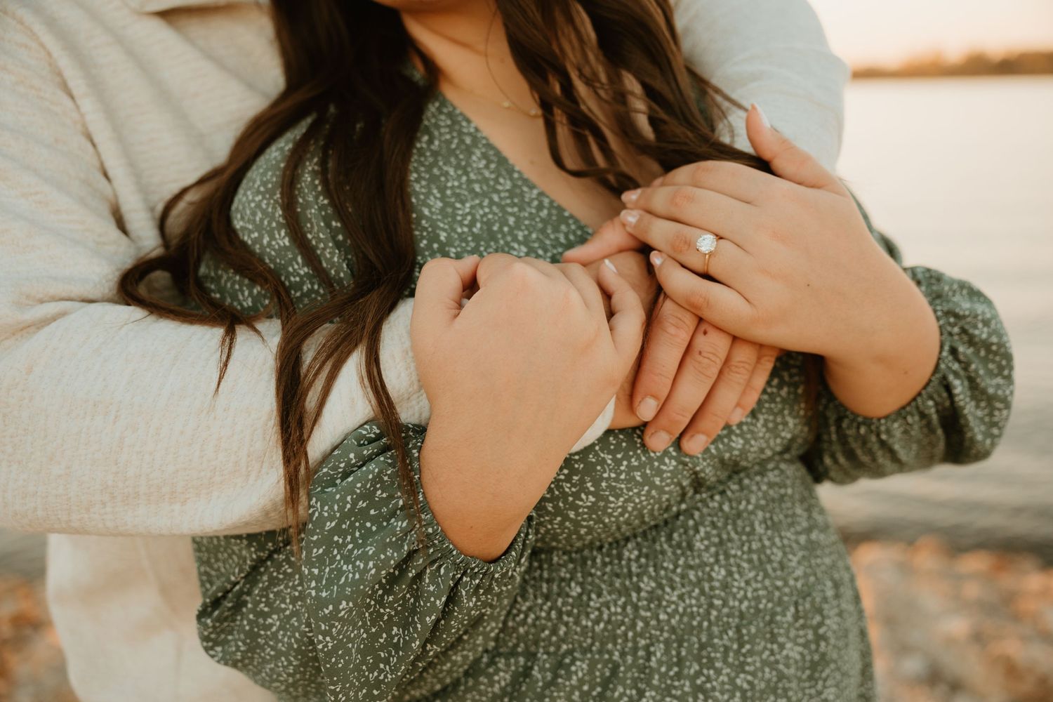 Close up of hands resting on a sage green dress in warm sunlight during a casual engagement photoshoot.