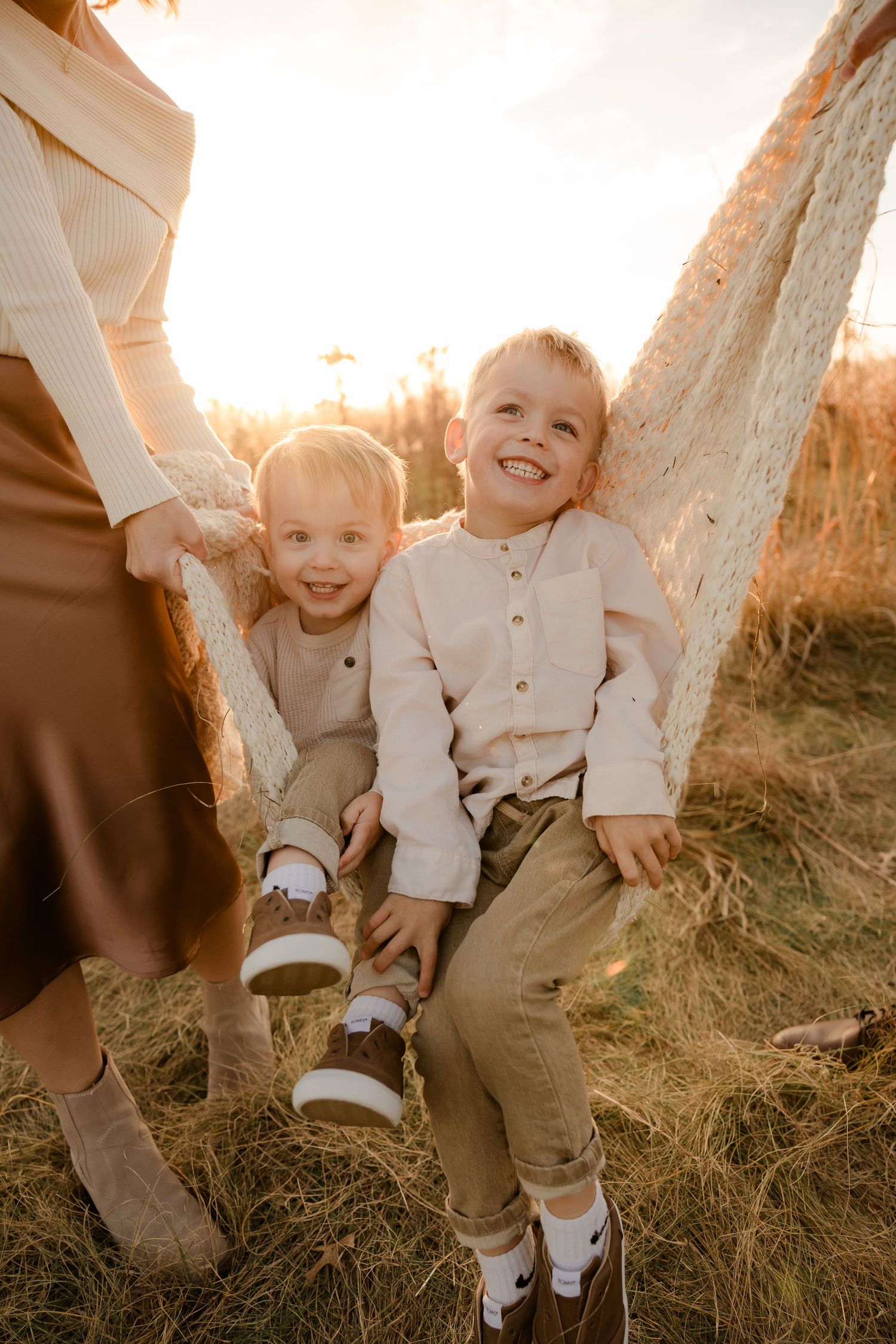 Heartwarming outdoor family moment at sunset with children sitting in grass wearing matching light-colored outfits.