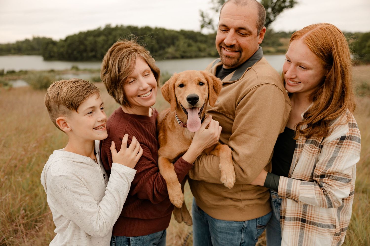 A golden retriever puppy is held lovingly by a family in a meadow on an autumn afternoon.