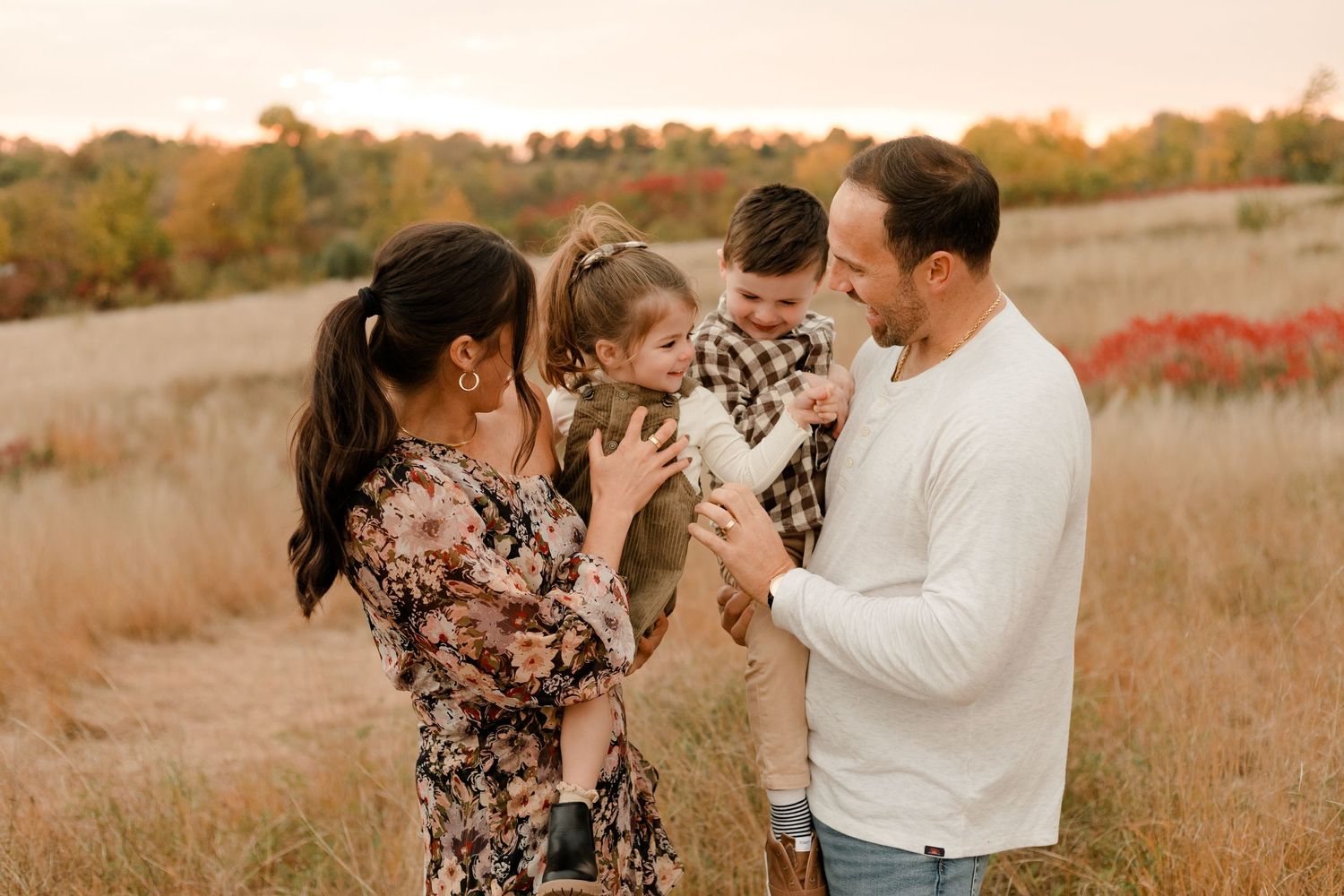 A family shares a tender moment together in an autumn field with golden grass and colorful fall foliage in the background.