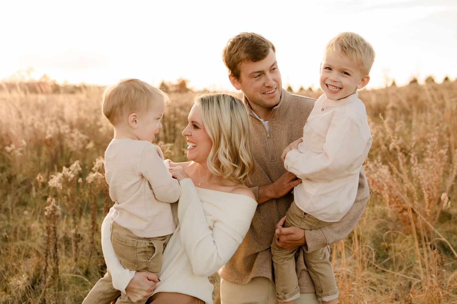 A warm family portrait in a golden field at sunset capturing a tender moment together in nature.