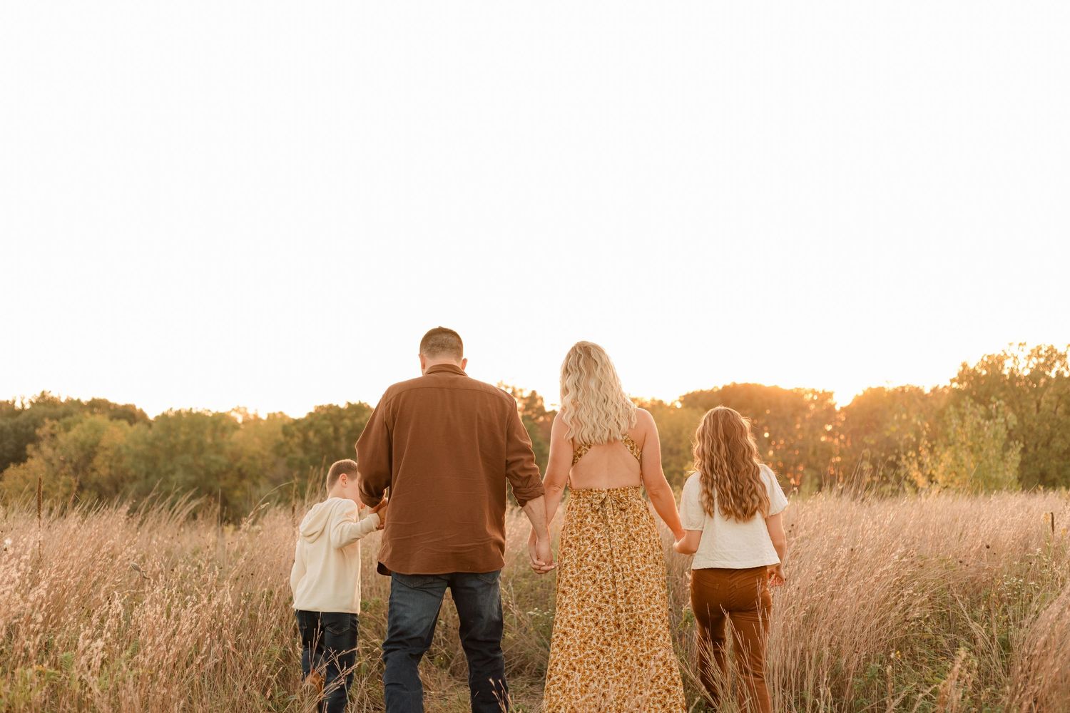 Family walking together through a golden prairie field at sunset during a photo session.